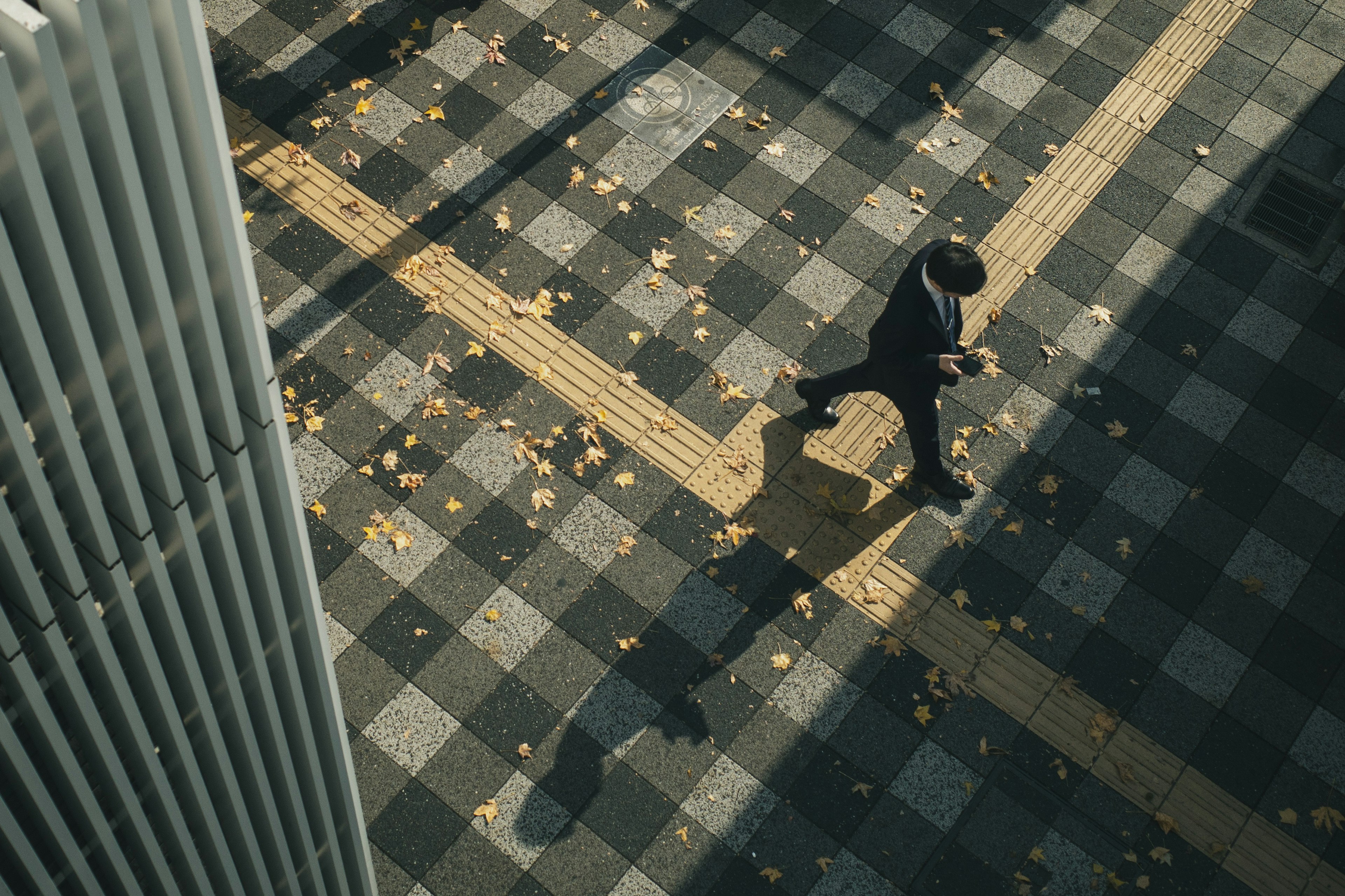 Hombre de negocios caminando sobre un pavimento a cuadros con hojas caídas