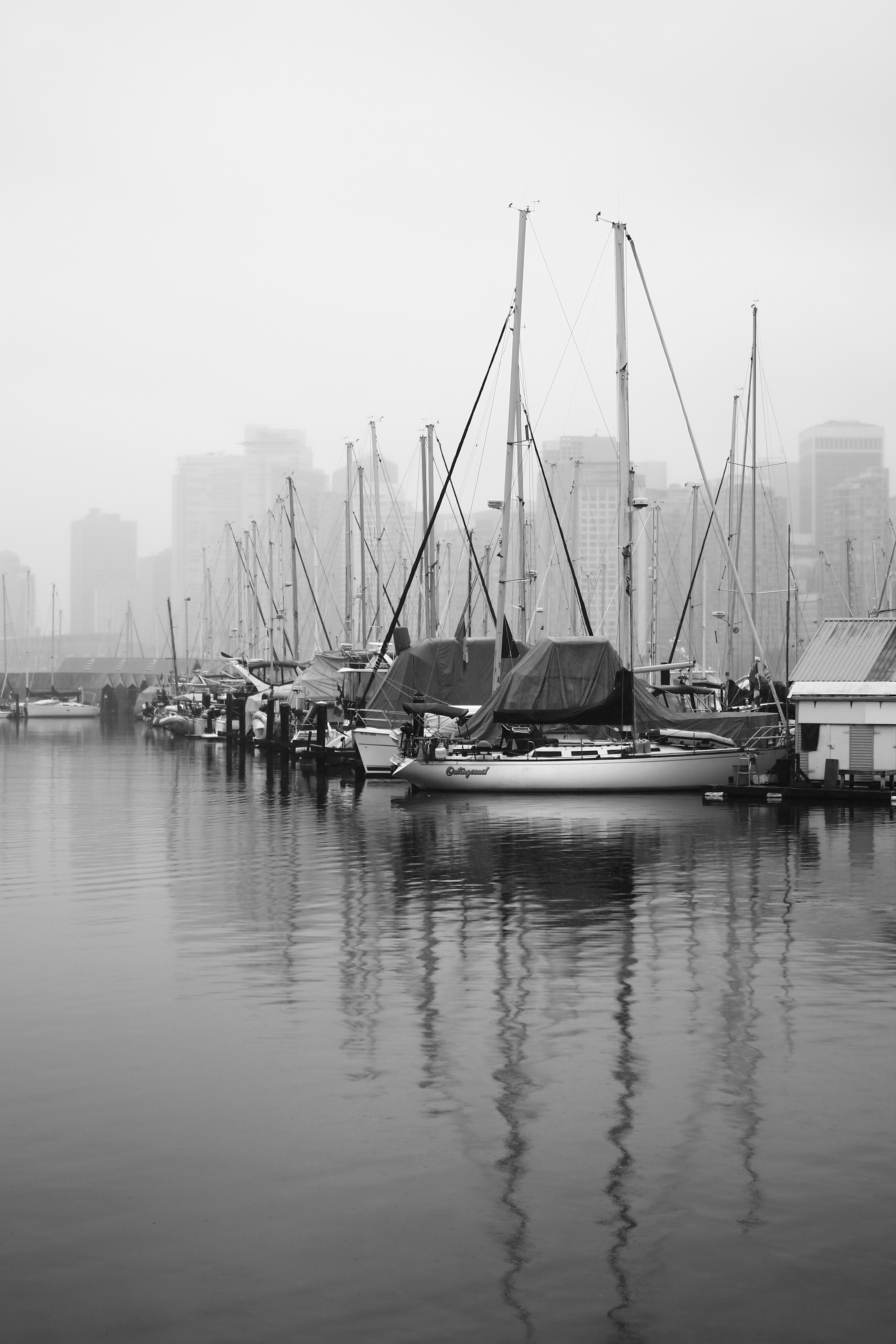 Puerto en blanco y negro con barcos y reflejos de rascacielos en la niebla