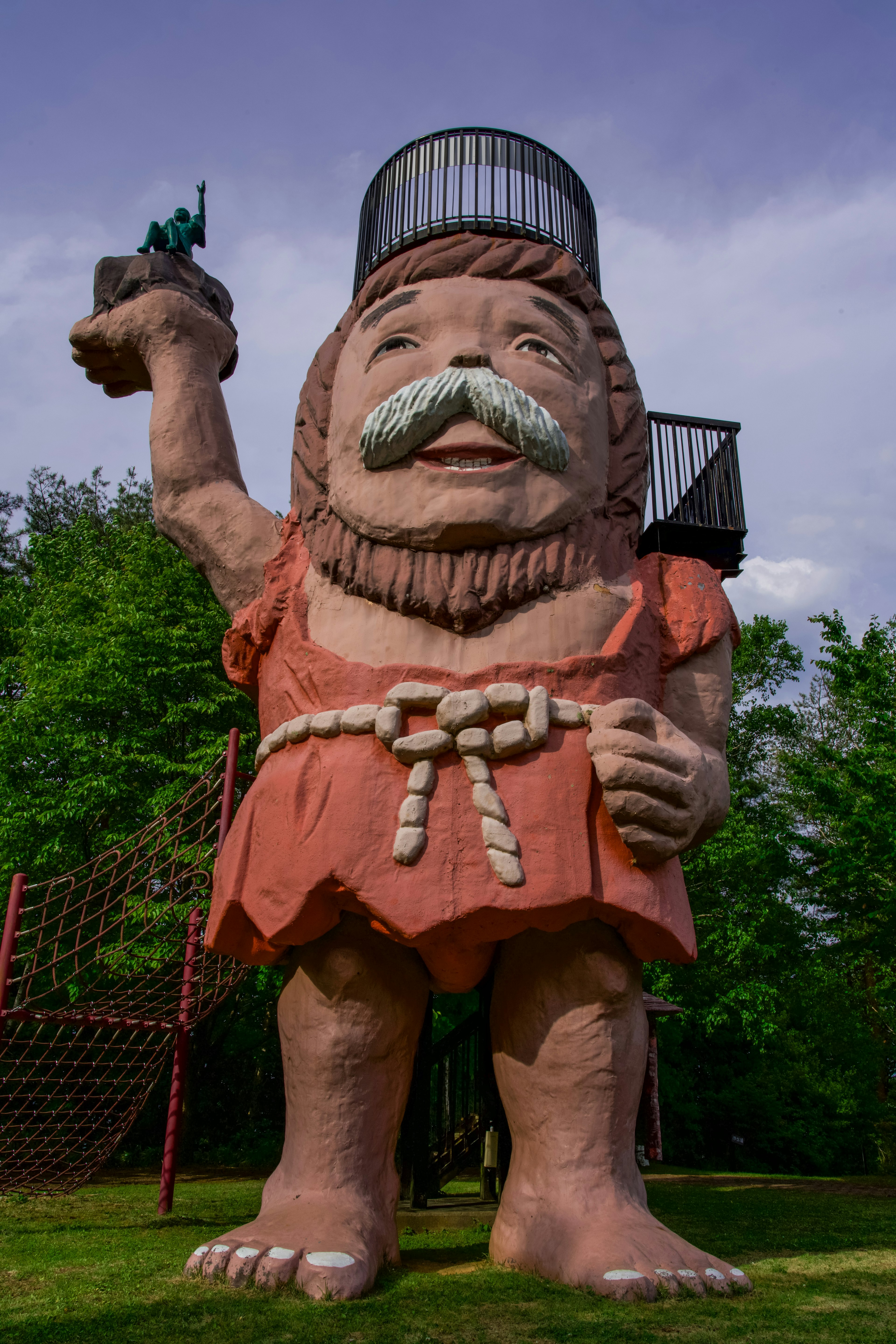 Eine riesige Statue eines Mannes, der eine kleine Figur in einer grünen Parklandschaft hält