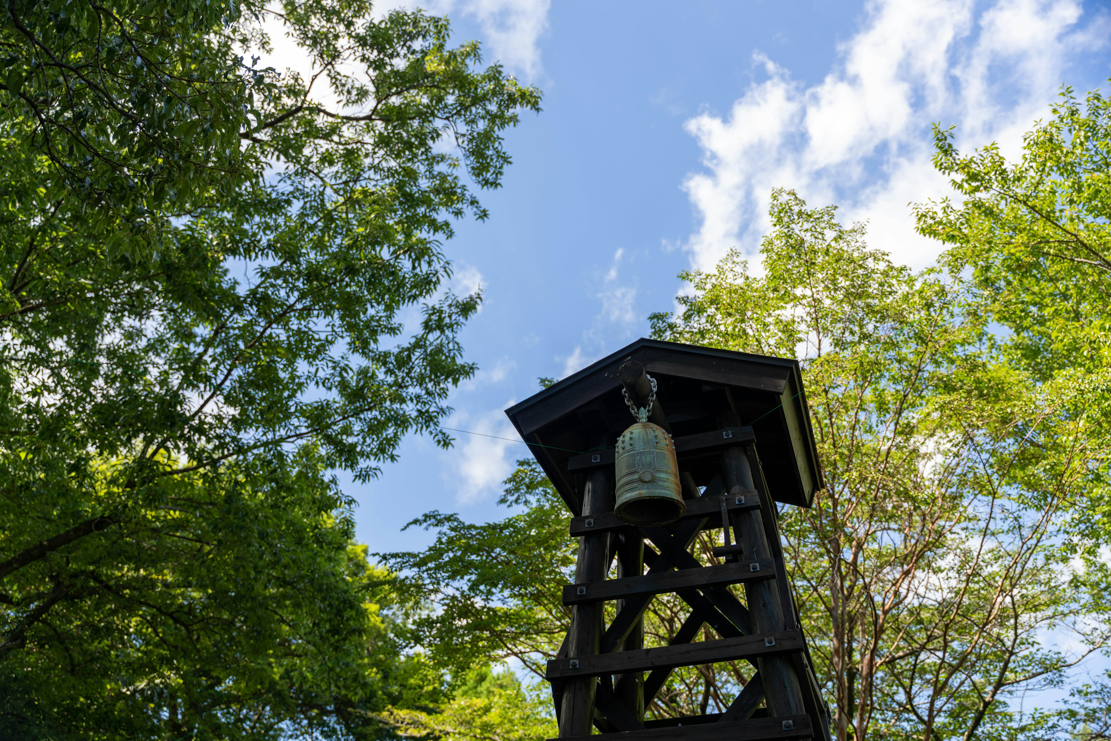 Tour de cloche en bois entourée d'arbres verts sous un ciel bleu