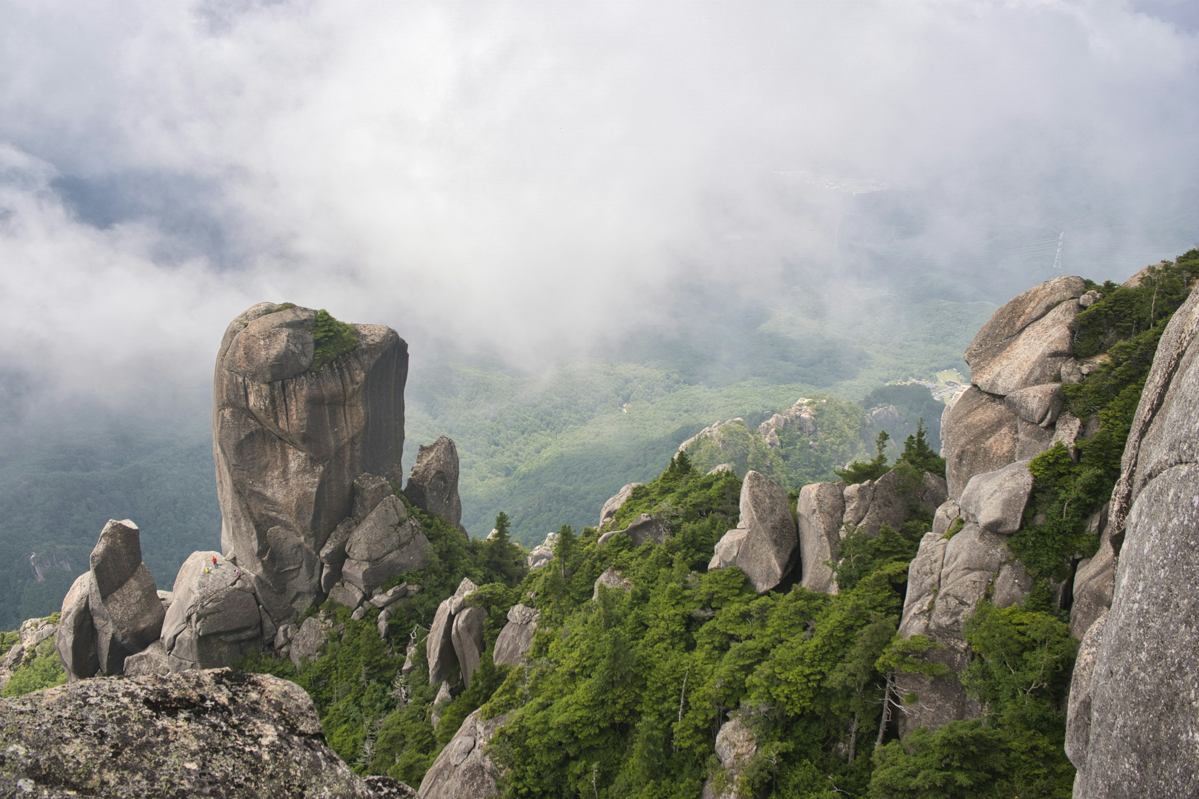 Mountain landscape shrouded in clouds featuring sharp rock formations and lush greenery