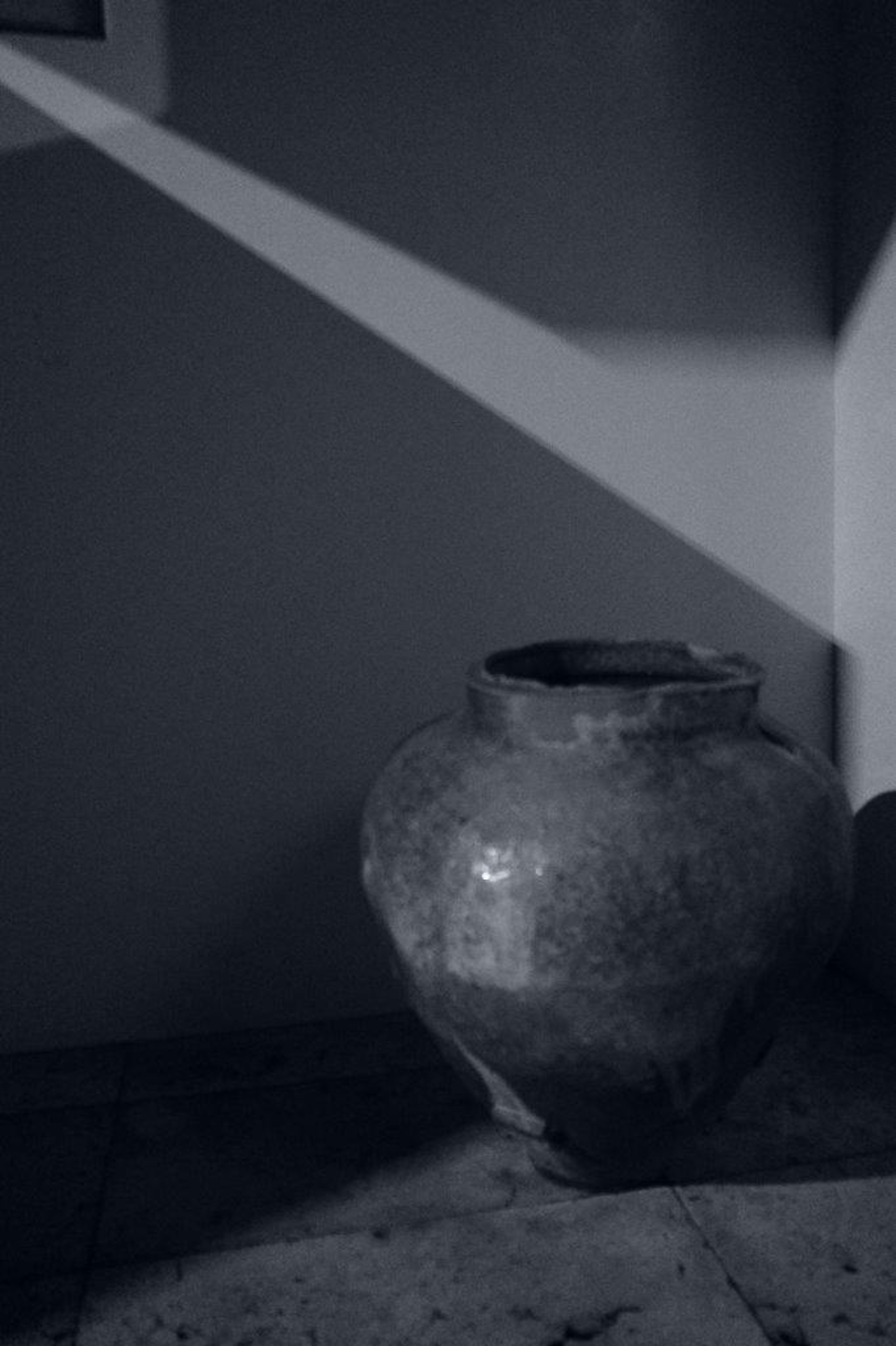 A ceramic pot placed against a dark background illuminated by diagonal light