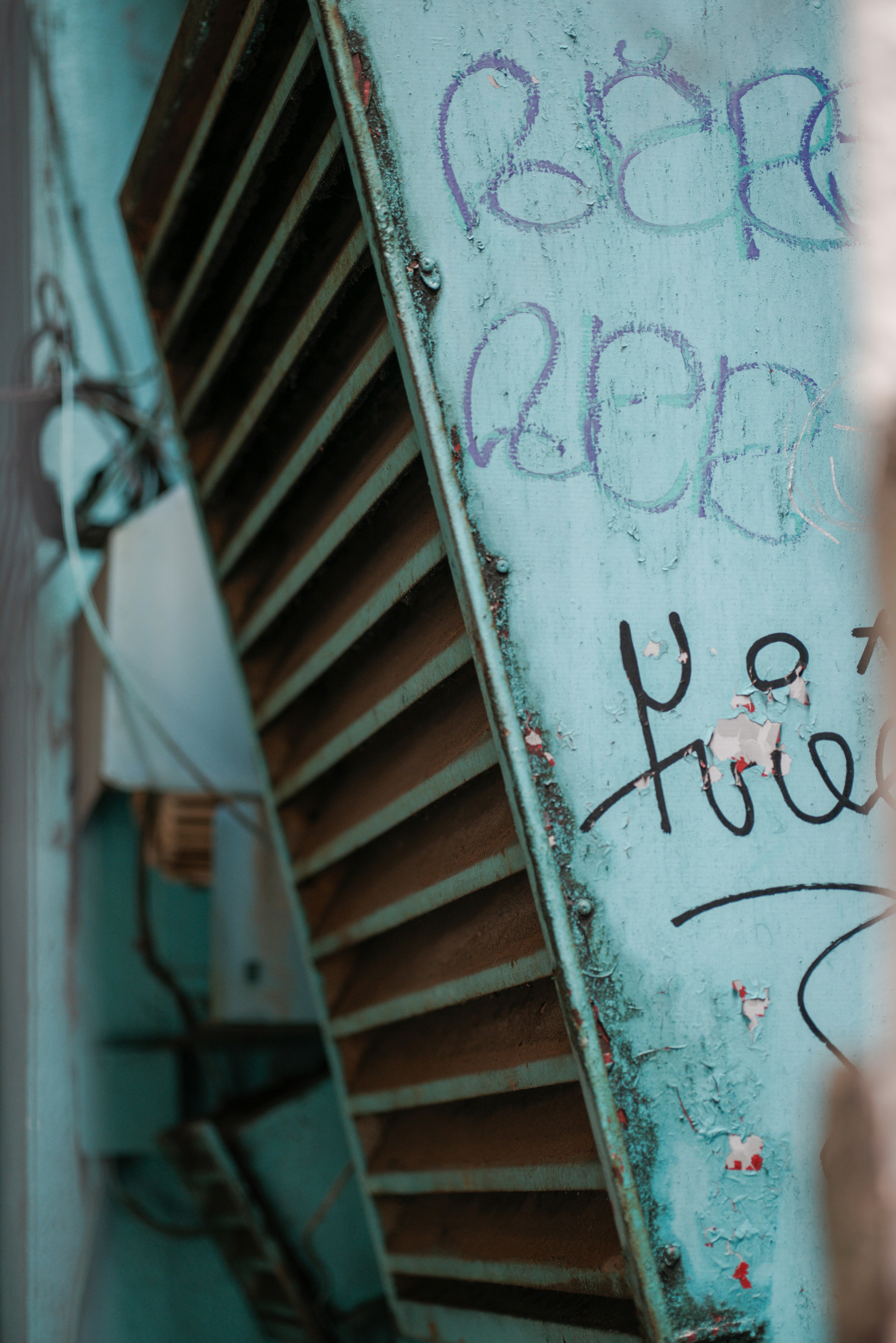 Gros plan d'une grille de ventilation montée sur un mur bleu avec des graffitis visibles