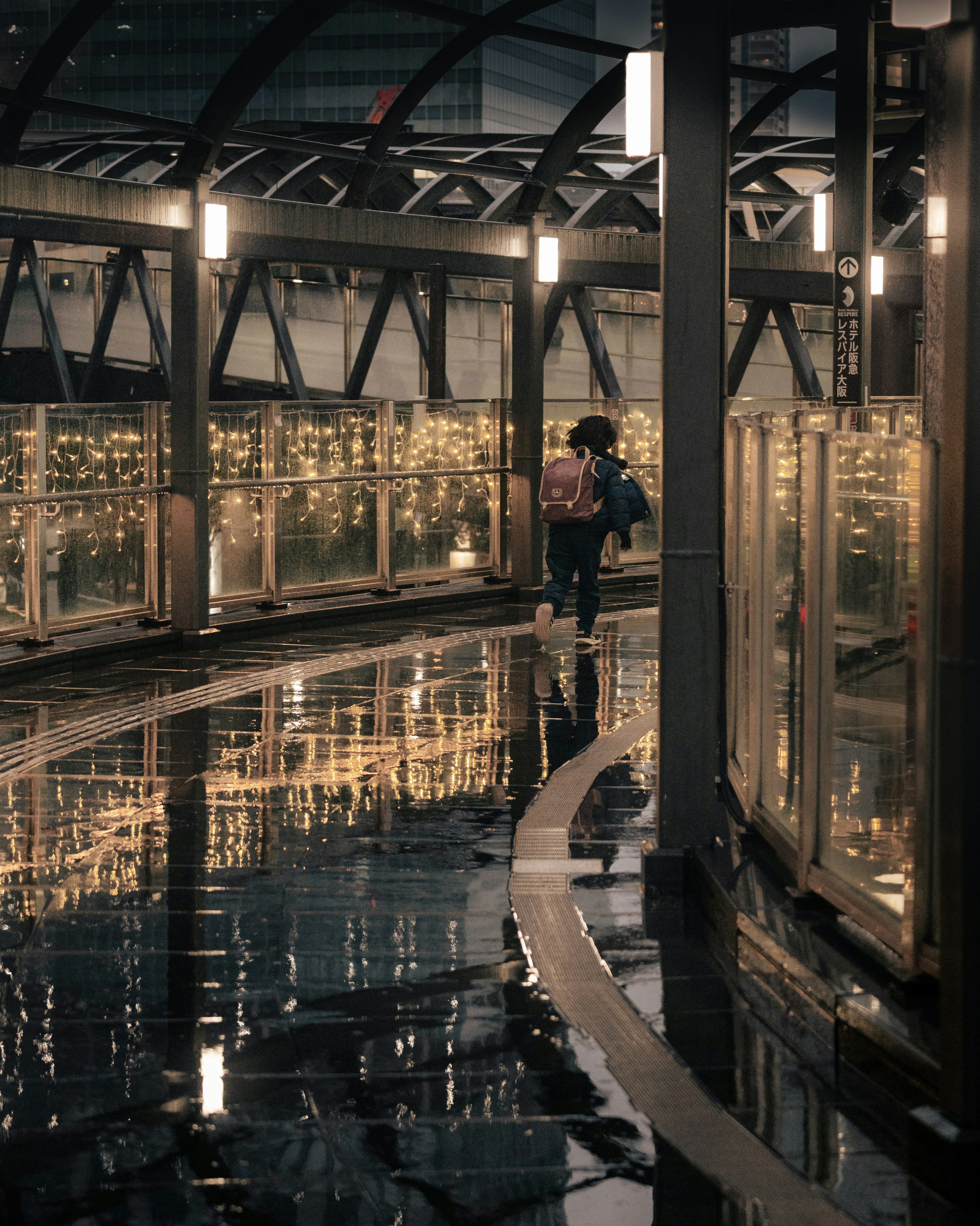 Person walking on a wet pathway with illuminated glass walls