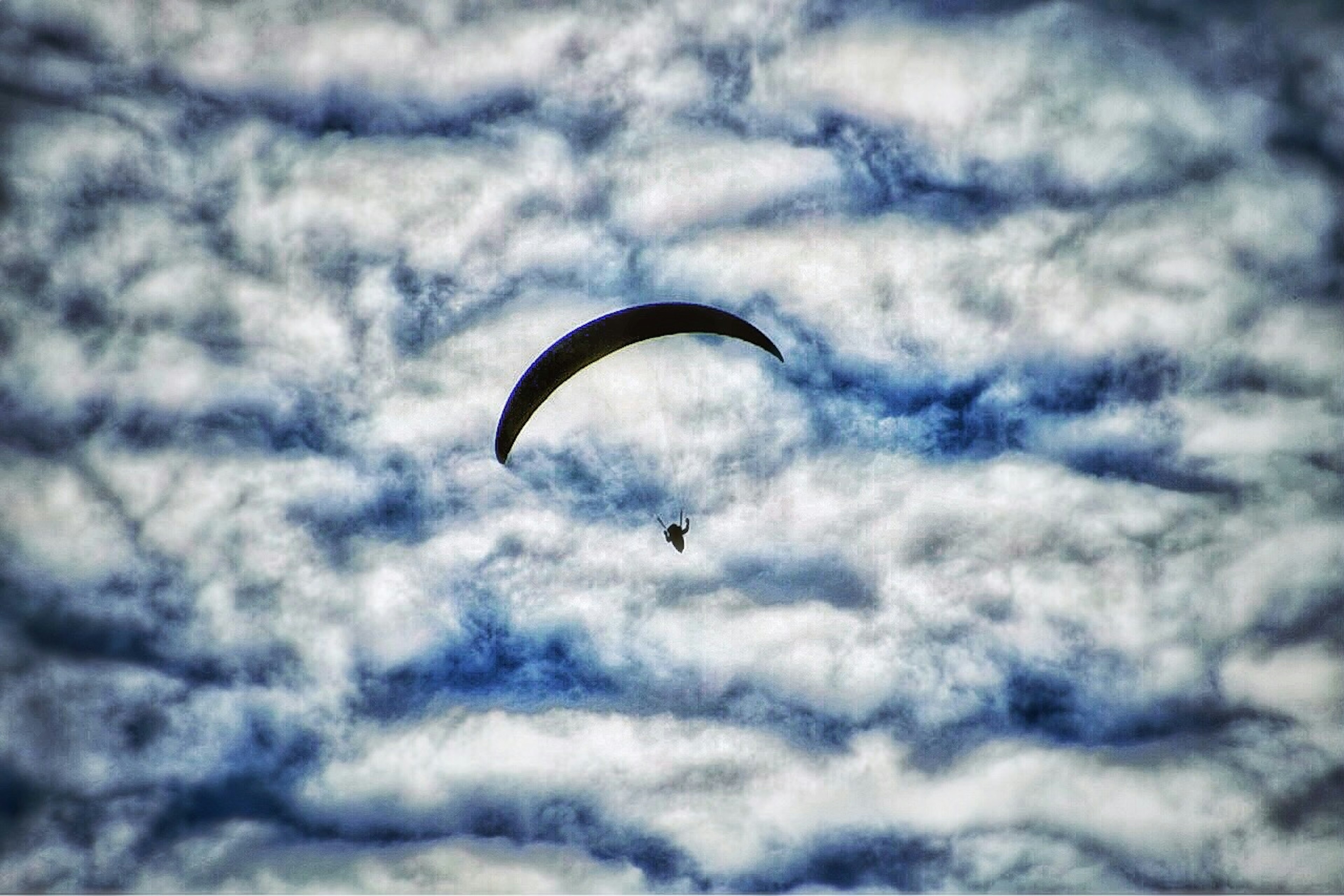 Sebuah paralayang hitam terbang di langit yang penuh awan