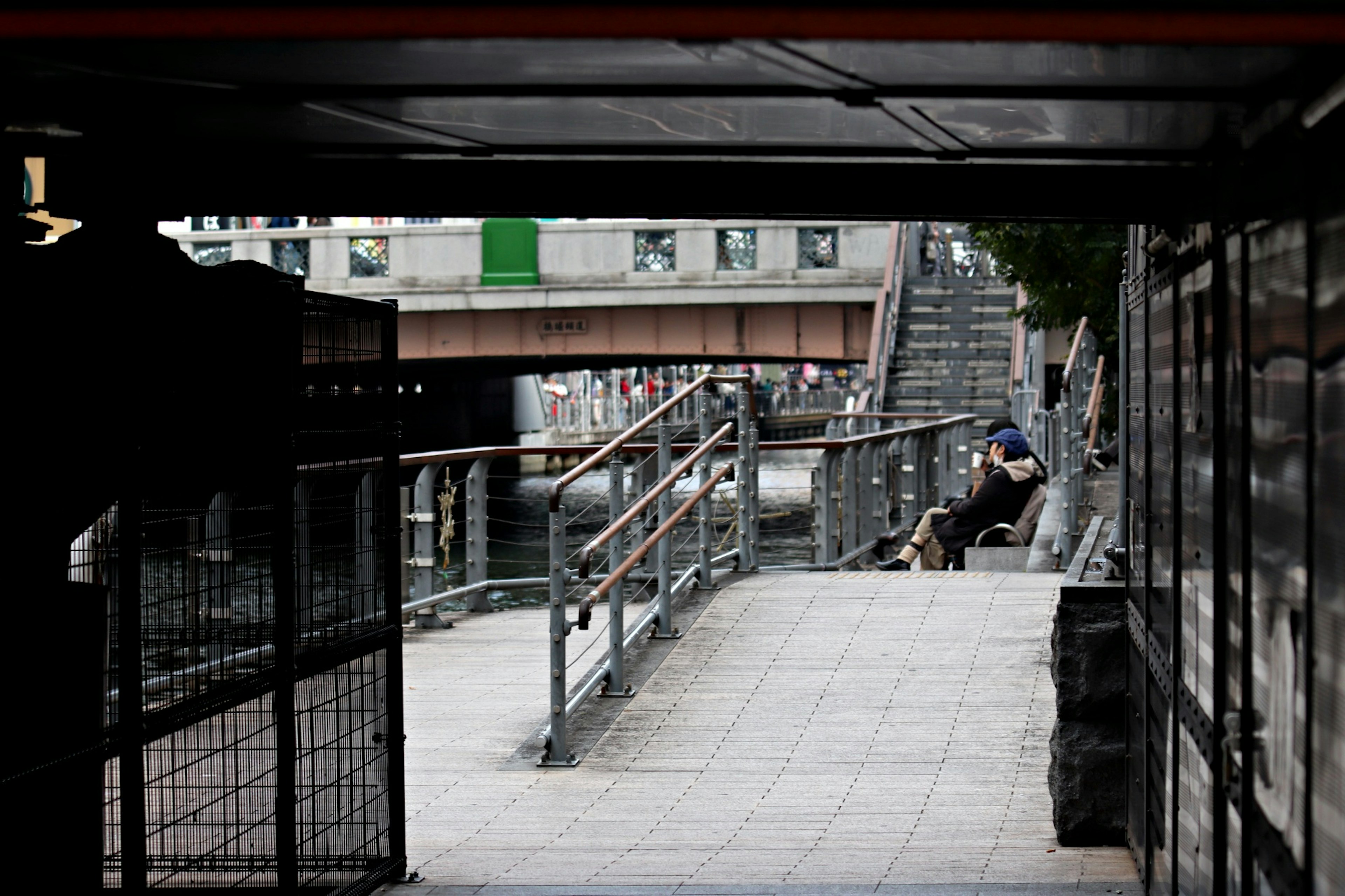 View of a riverside walkway and bridge from a dark tunnel