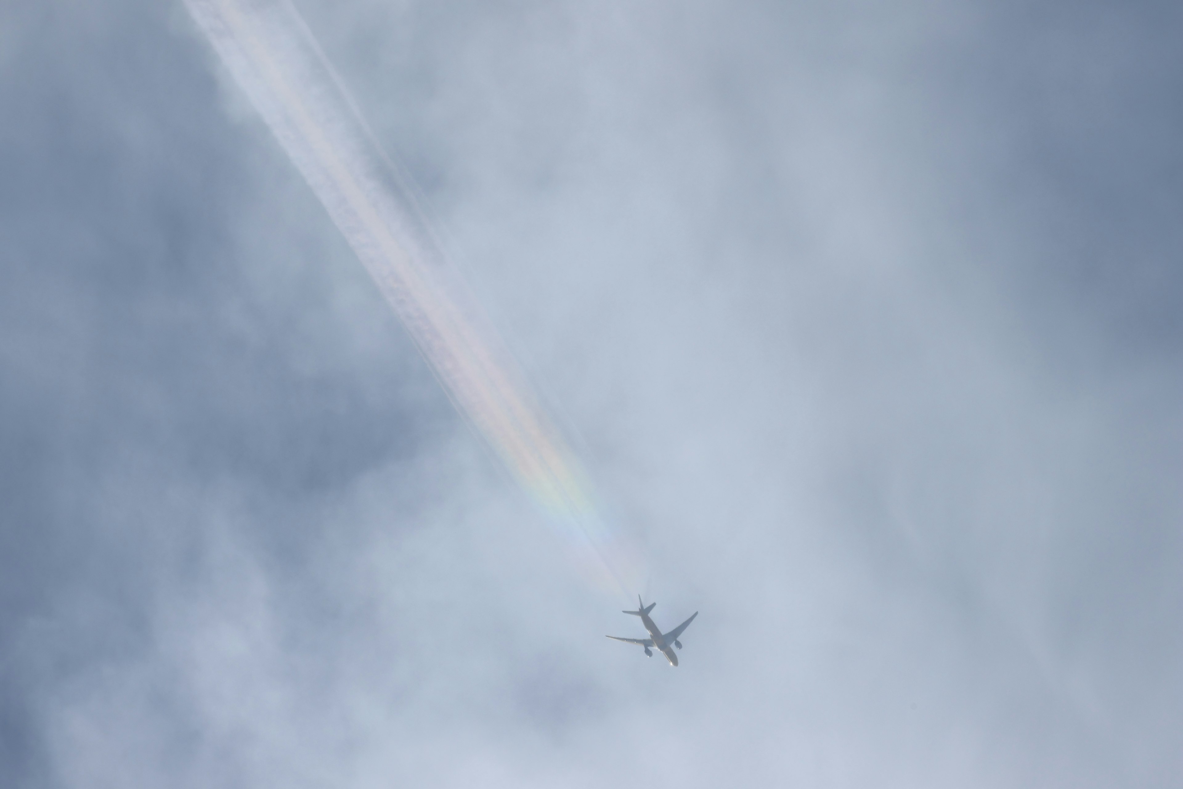 Flugzeug fliegt im blauen Himmel mit einem Regenbogen-Kondensstreifen