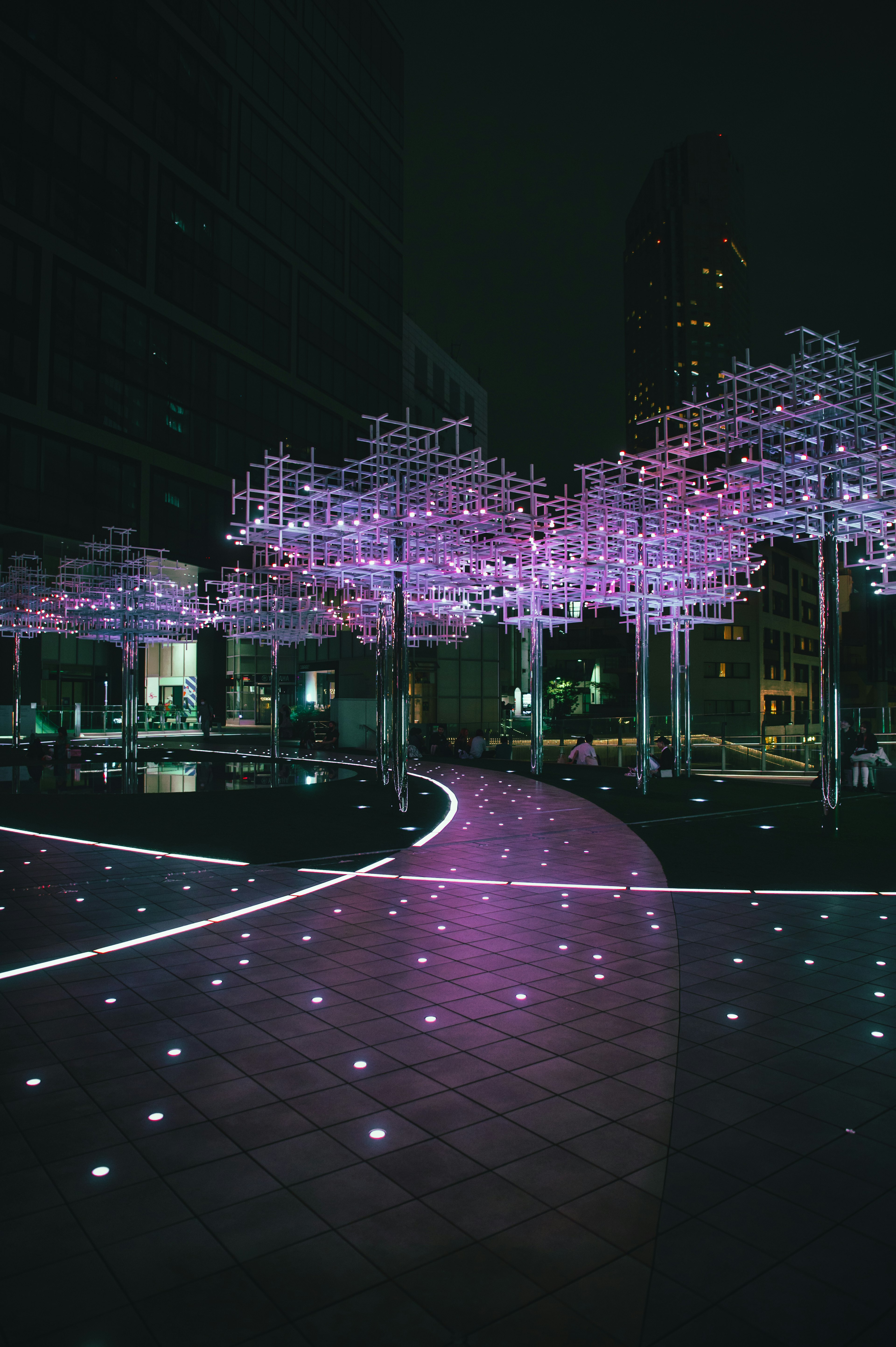 A park scene with trees adorned in purple lights at night