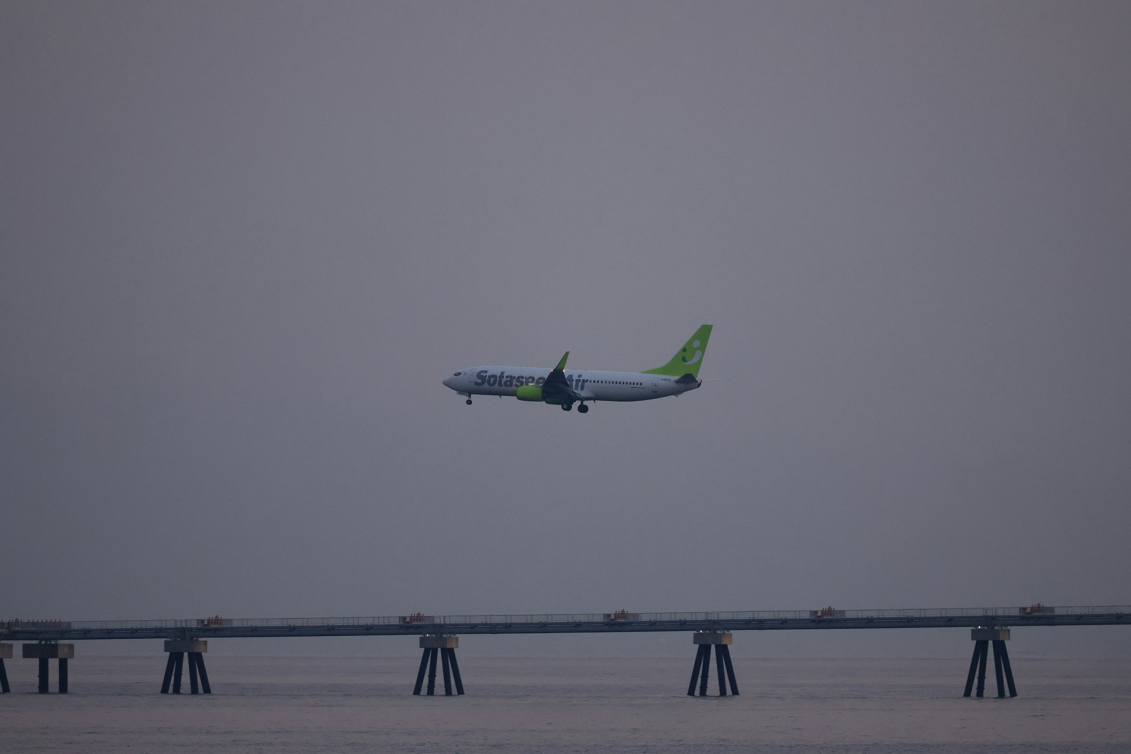 Flugzeug fliegt über eine Brücke in einem grauen Himmel