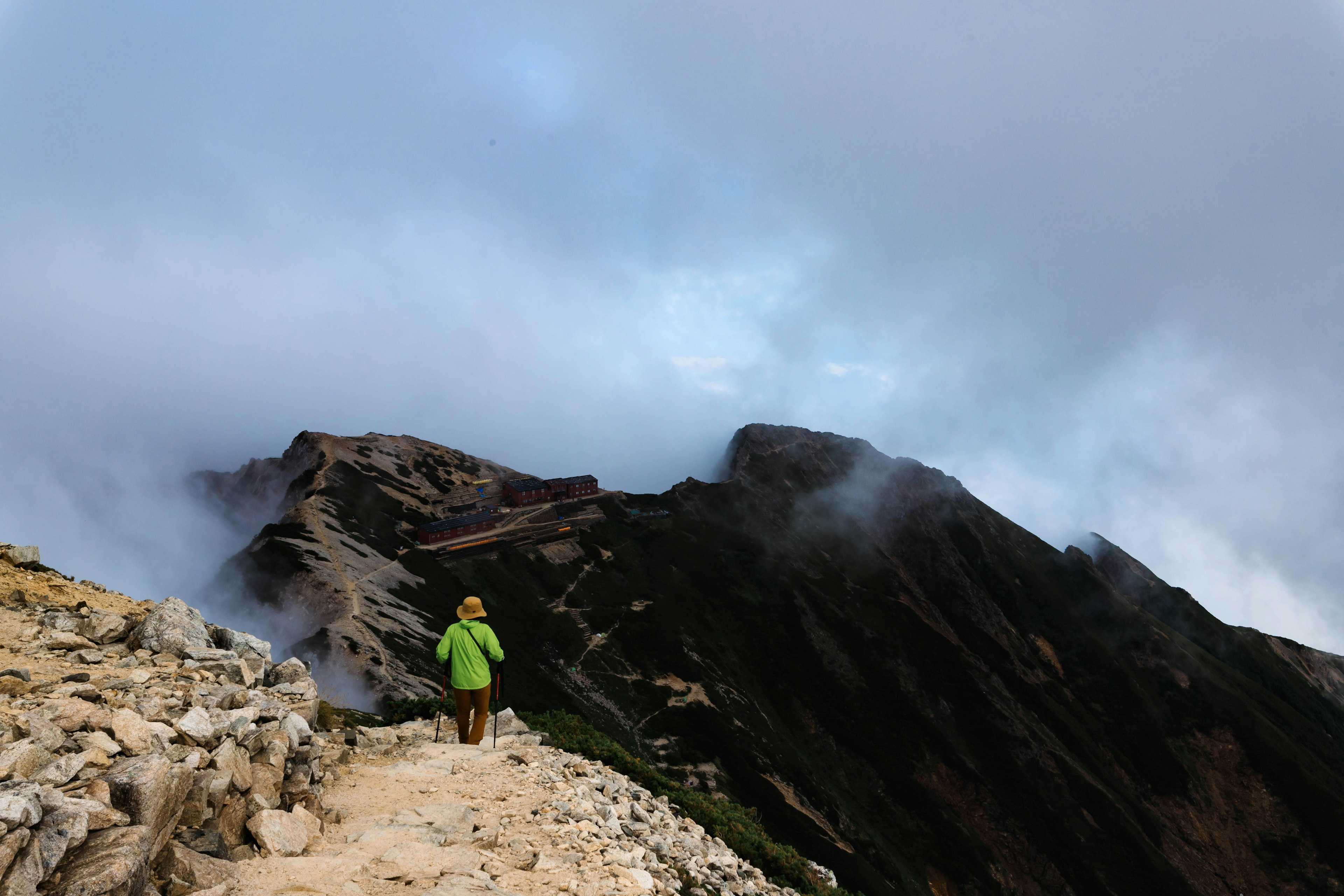 Wanderer in grüner Kleidung, der einen nebligen Bergpfad entlanggeht