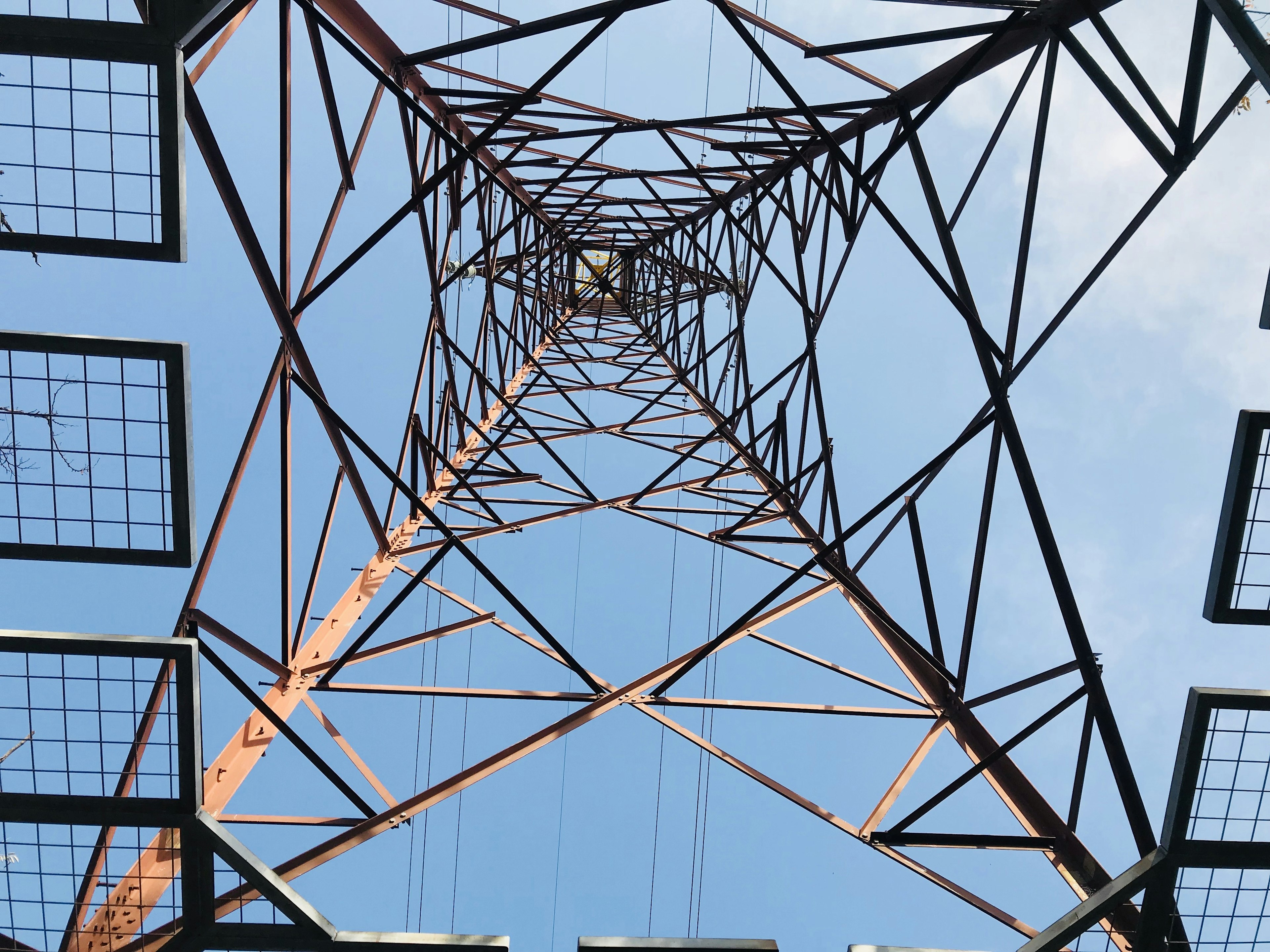 View looking up from beneath a transmission tower with a blue sky