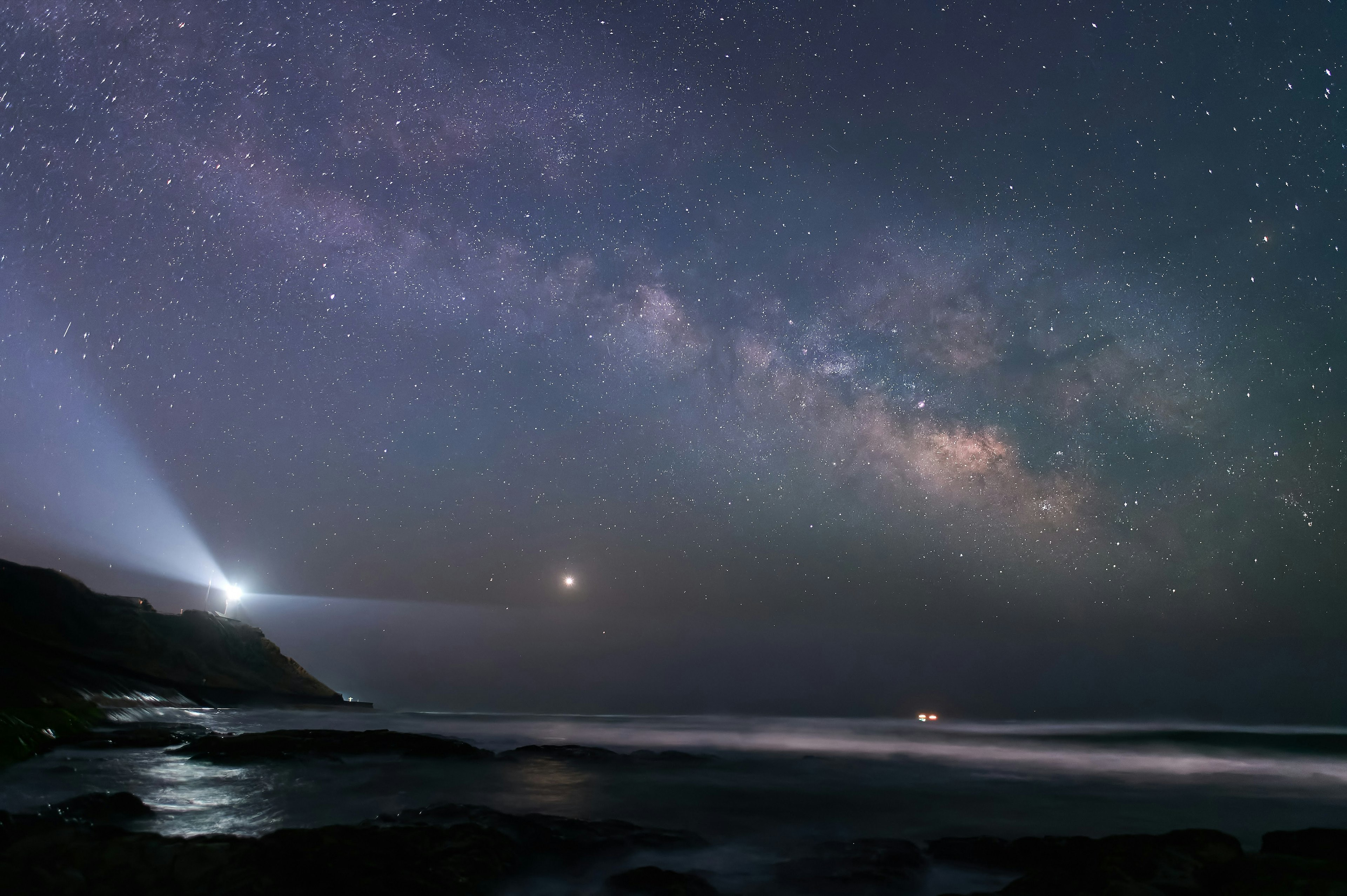 Vista escénica del océano bajo un cielo estrellado con un faro y la Vía Láctea brillando intensamente