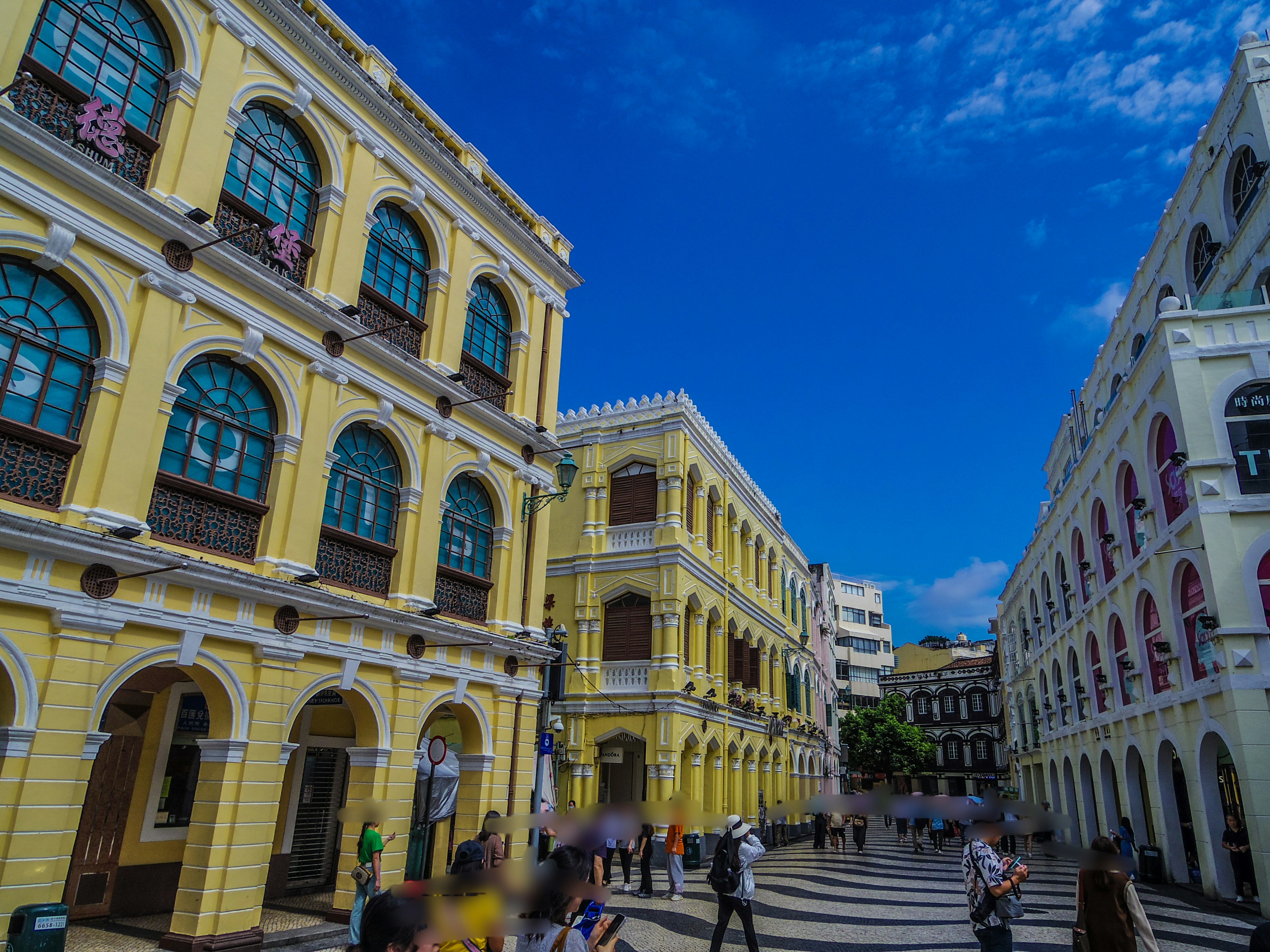 Bunte Gebäude auf einem Platz in Macau mit blauem Himmel und vorbeigehenden Menschen