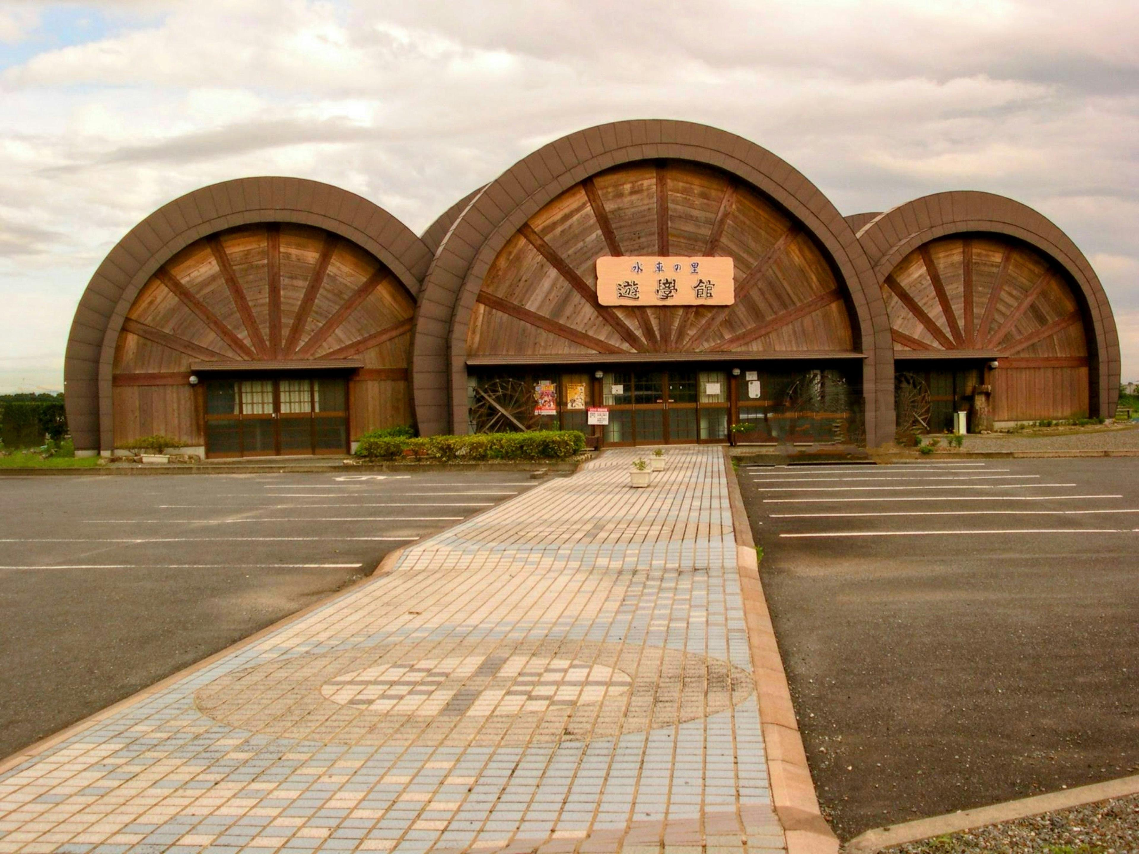 Exterior view of a building with unique arch-shaped roofs featuring a parking lot and a tiled walkway