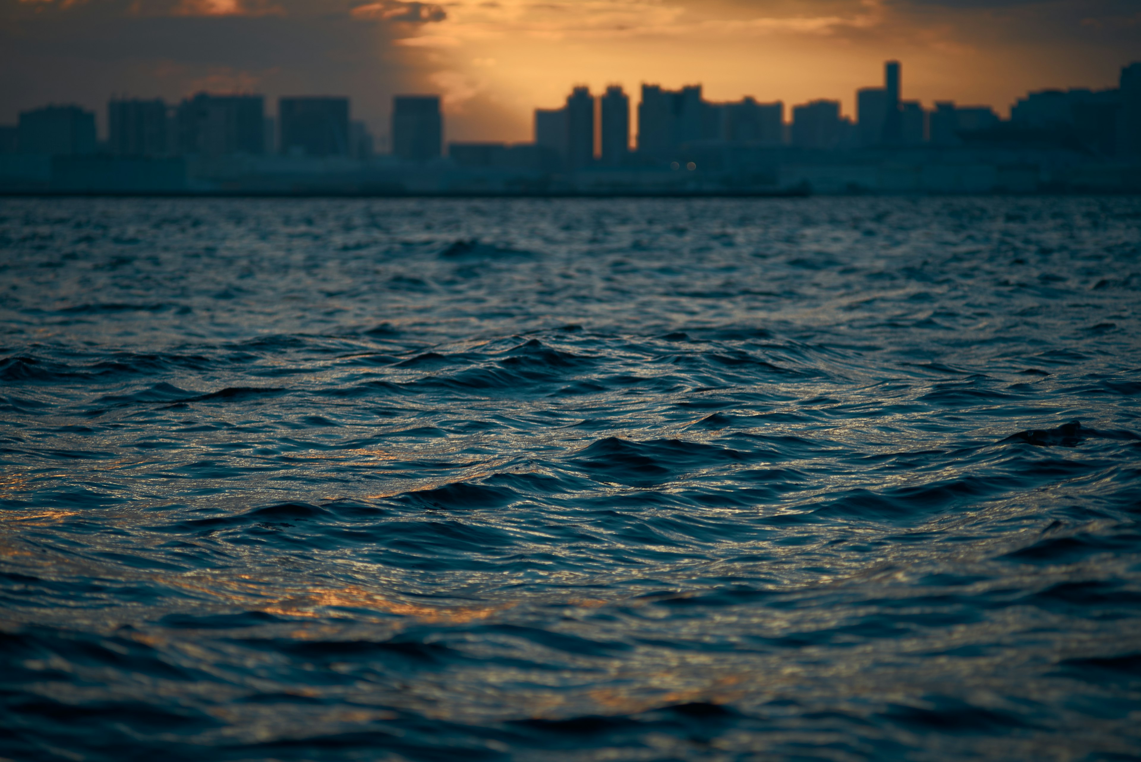 夕日を背景にした都市のシルエットと波のある水面