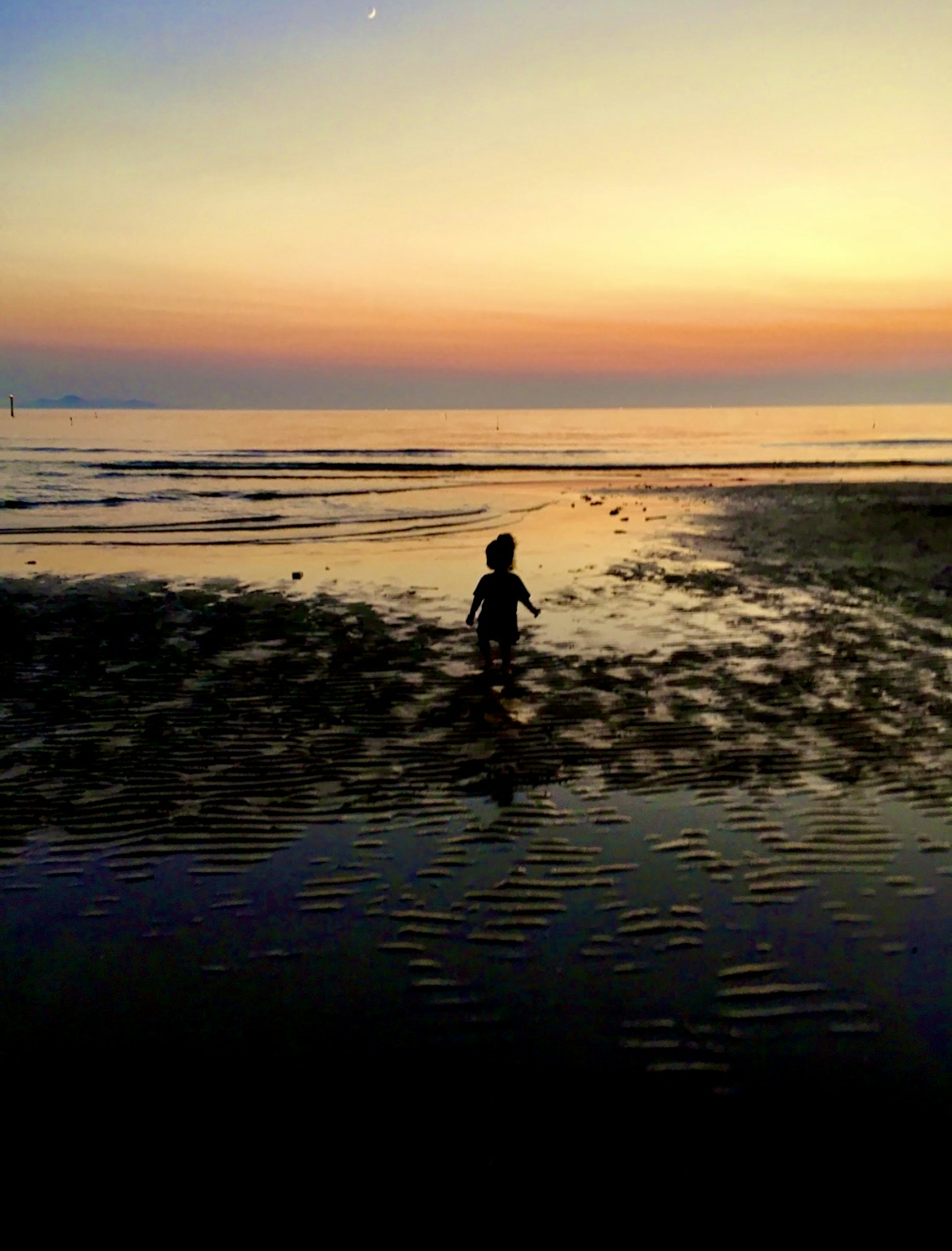 Silhouette d'un enfant jouant sur la plage à contre-jour au coucher de soleil