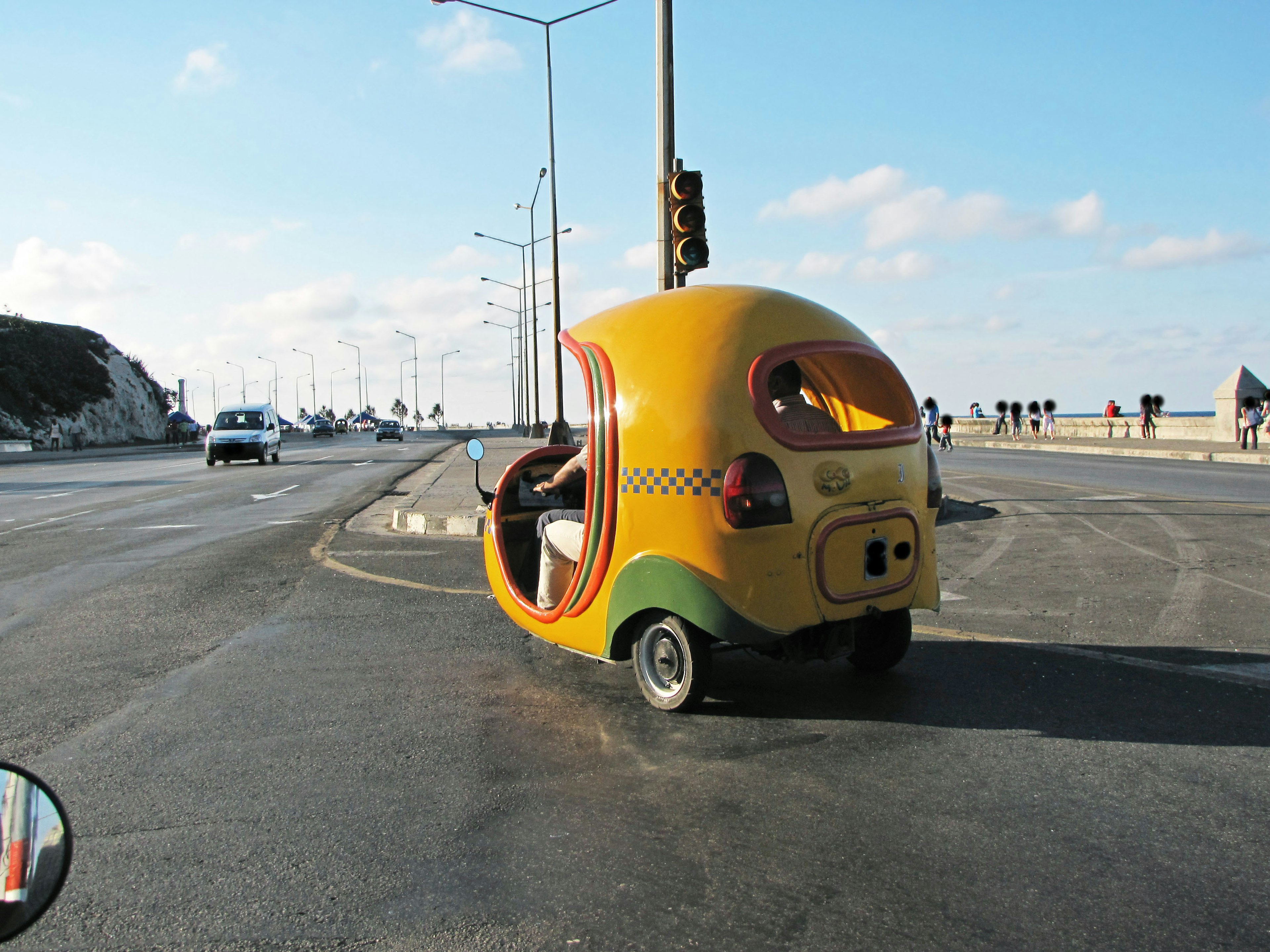 A colorful taxi-like small vehicle is stopped at a road intersection