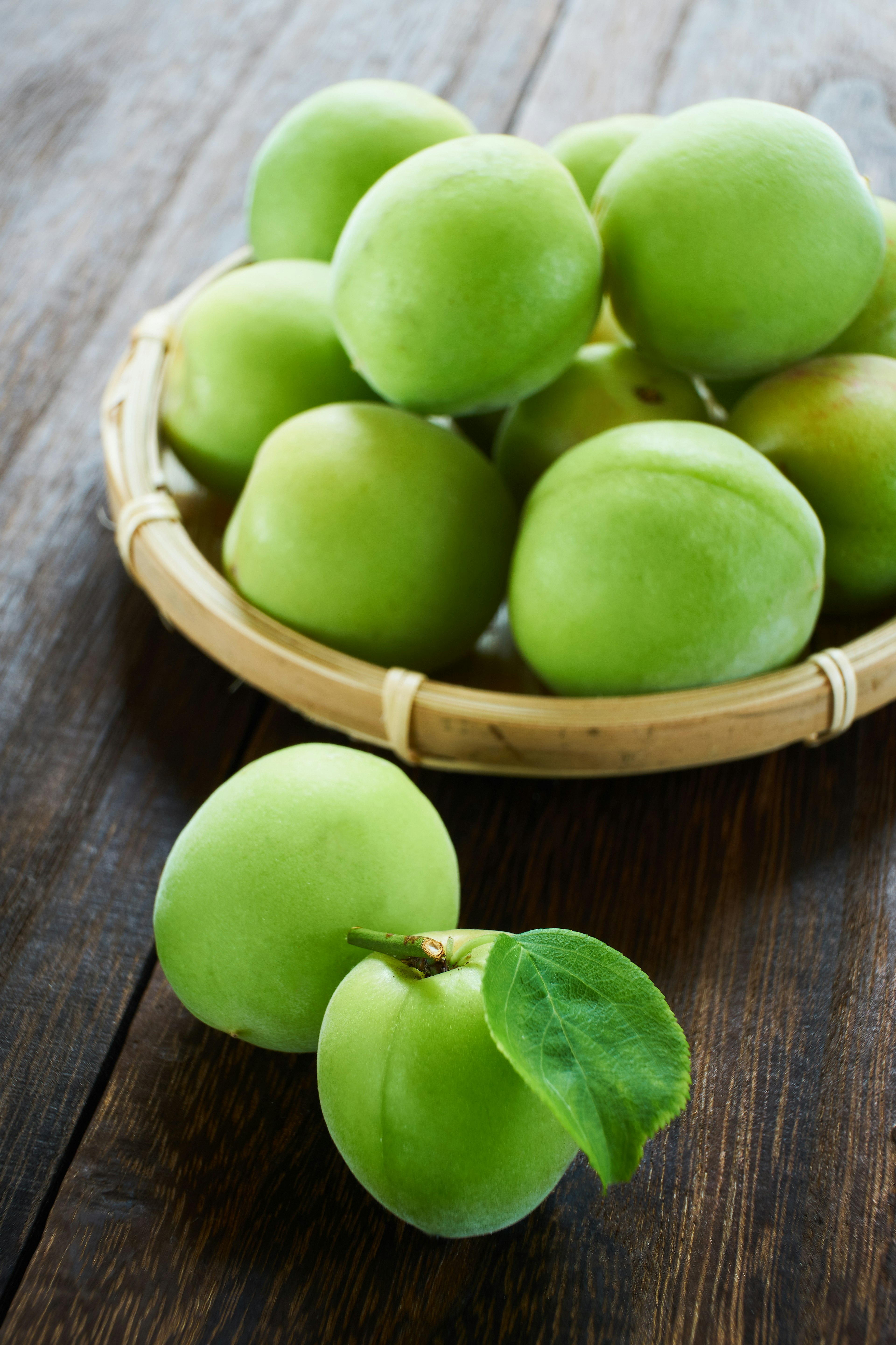 Plum hijau dalam keranjang bambu di atas meja kayu