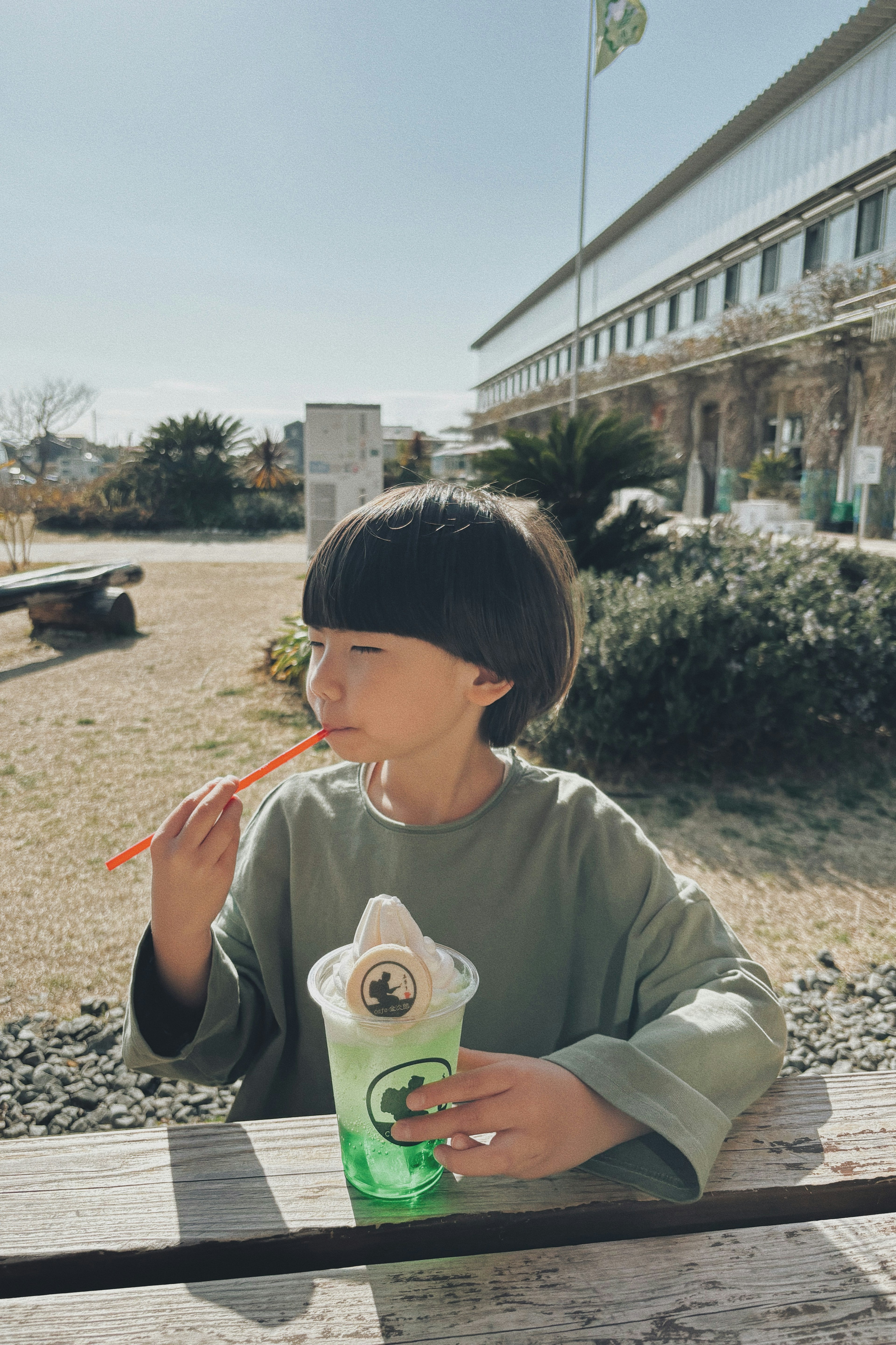 Bambino che gusta una bevanda verde con una cannuccia in una giornata di sole in un parco