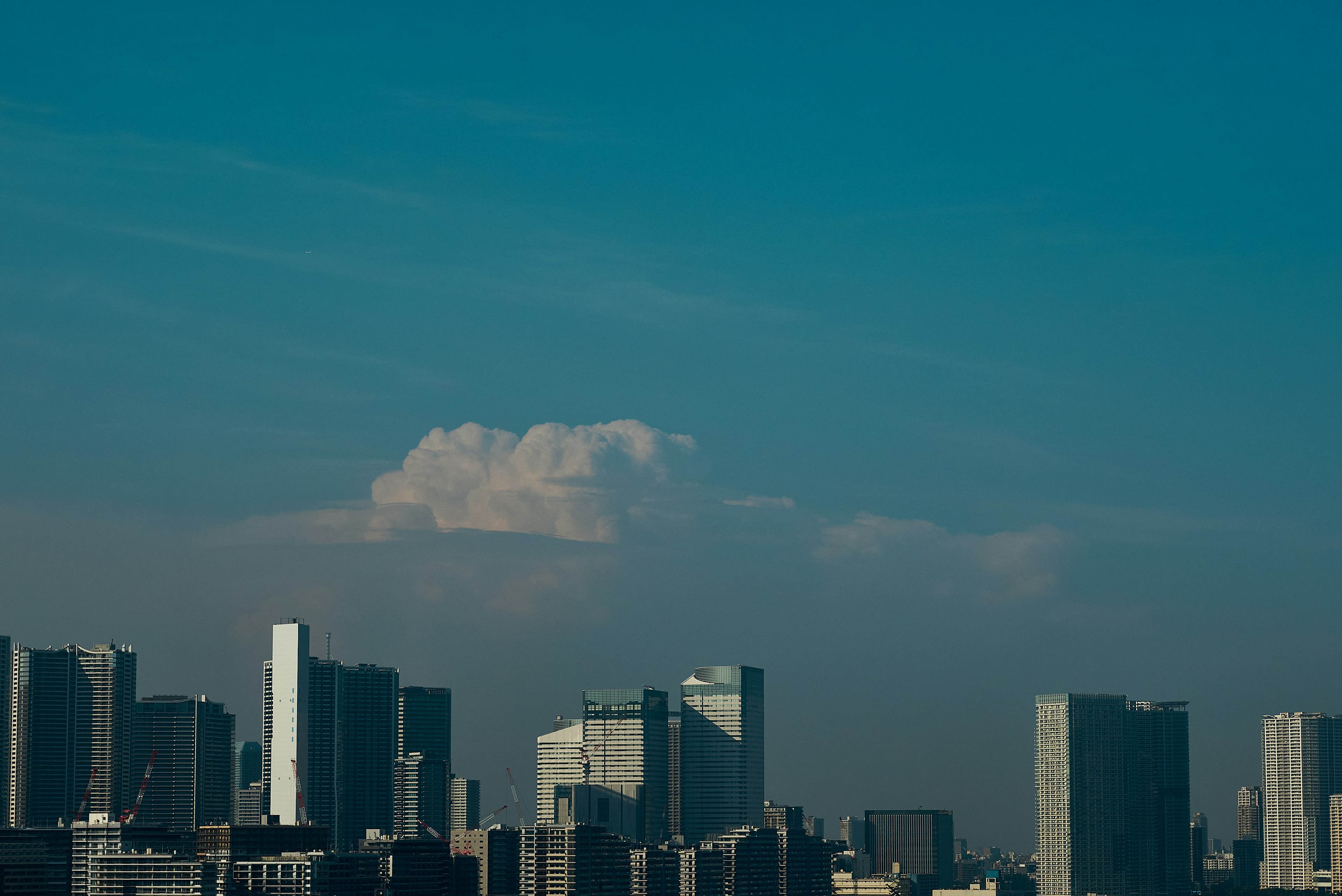 City skyline with tall buildings under a blue sky and fluffy clouds