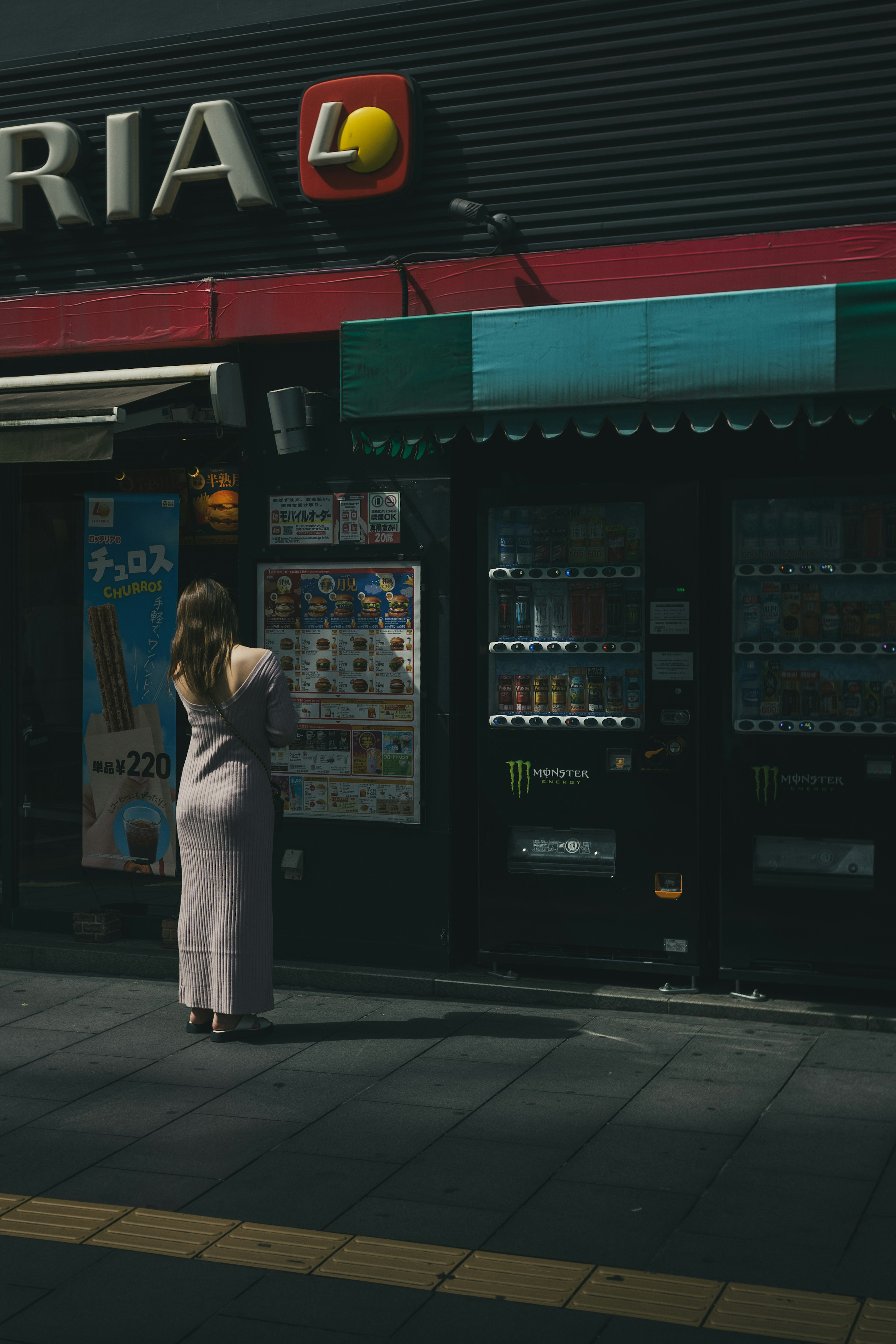 一名女性站在自動販賣機前，背景是商店