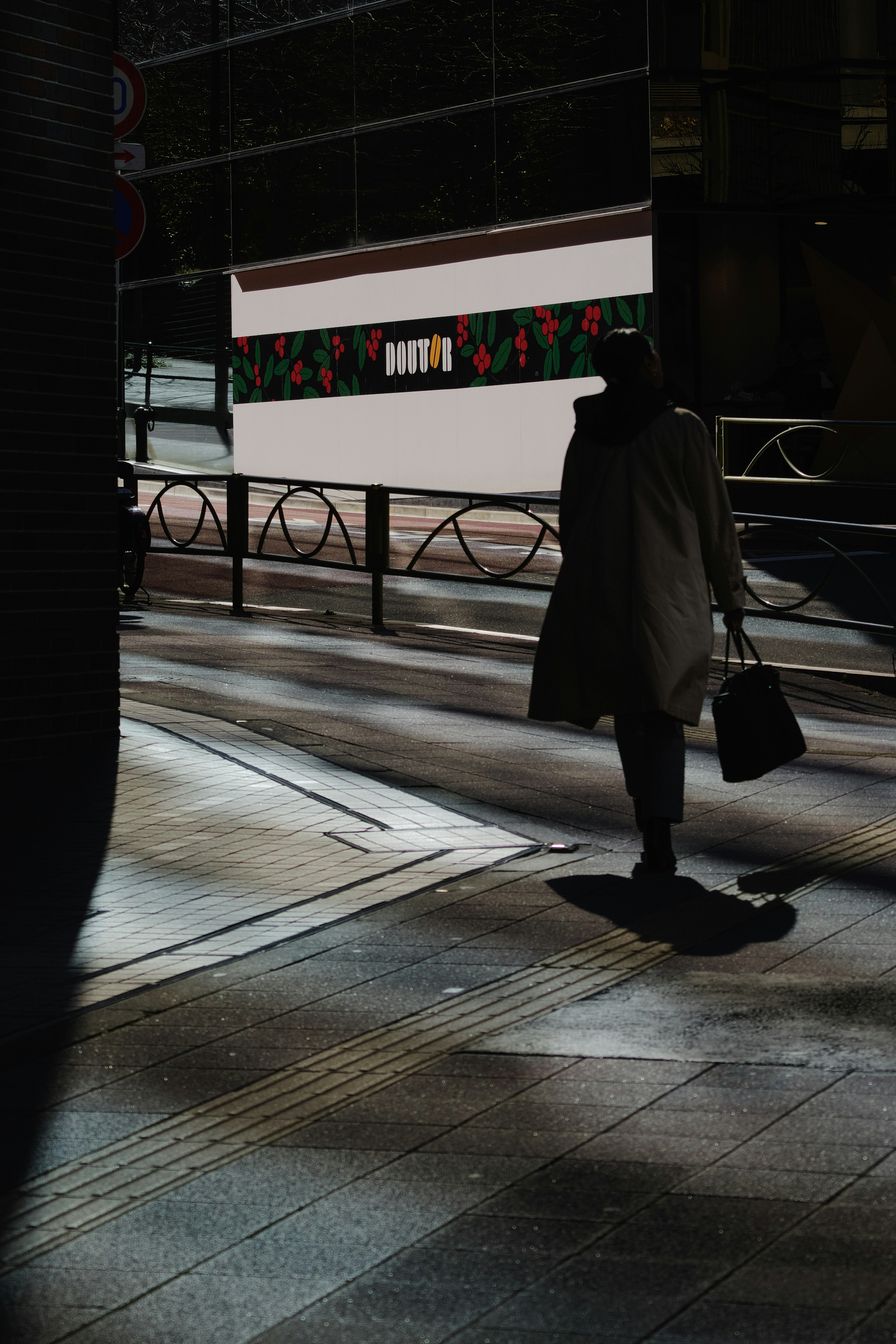 Silhouette einer Frau, die an einer schwach beleuchteten Straßenecke geht, mit einem hellen Hintergrund und kontrastierenden Schatteneffekten