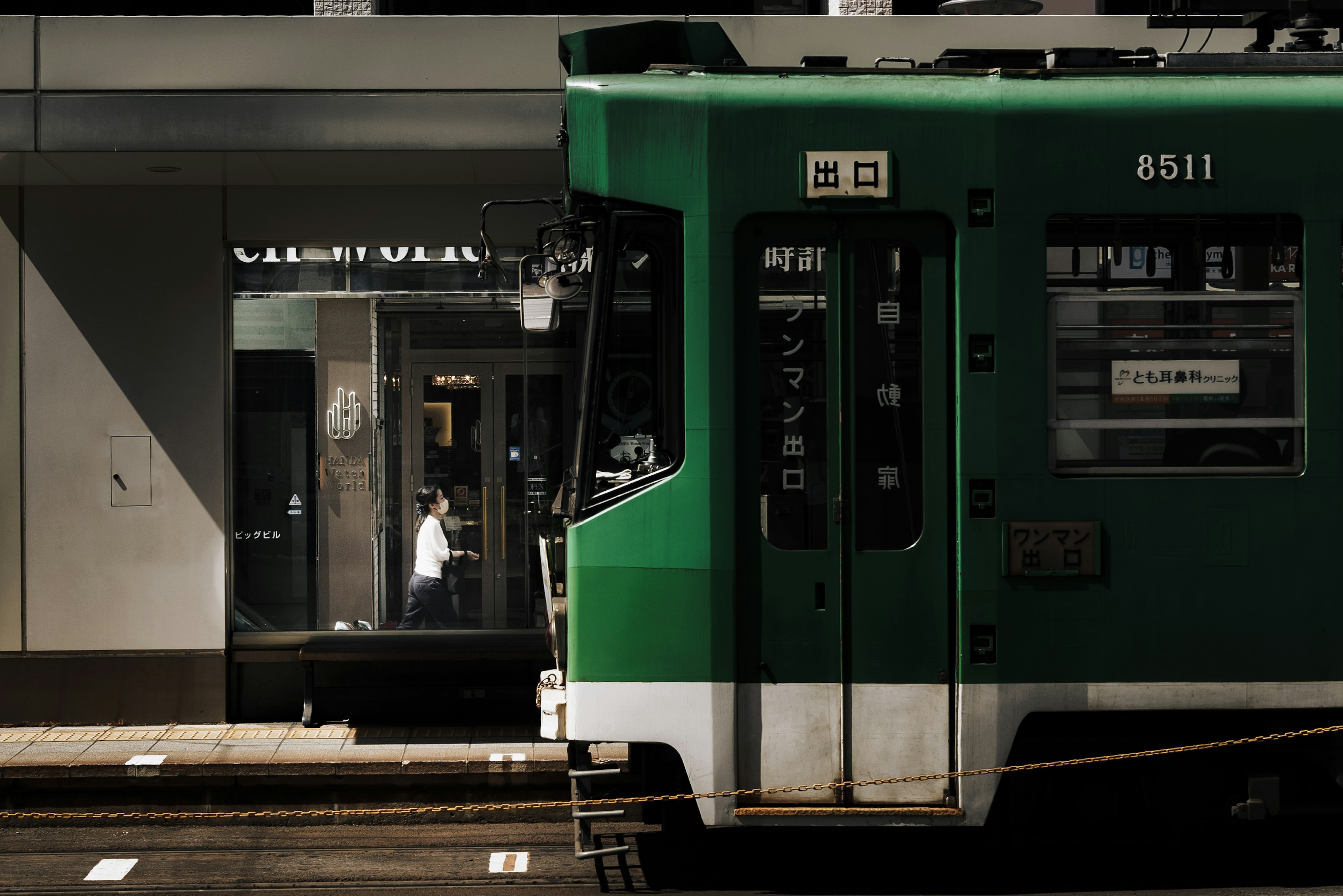 Green tram alongside a store window in an urban setting