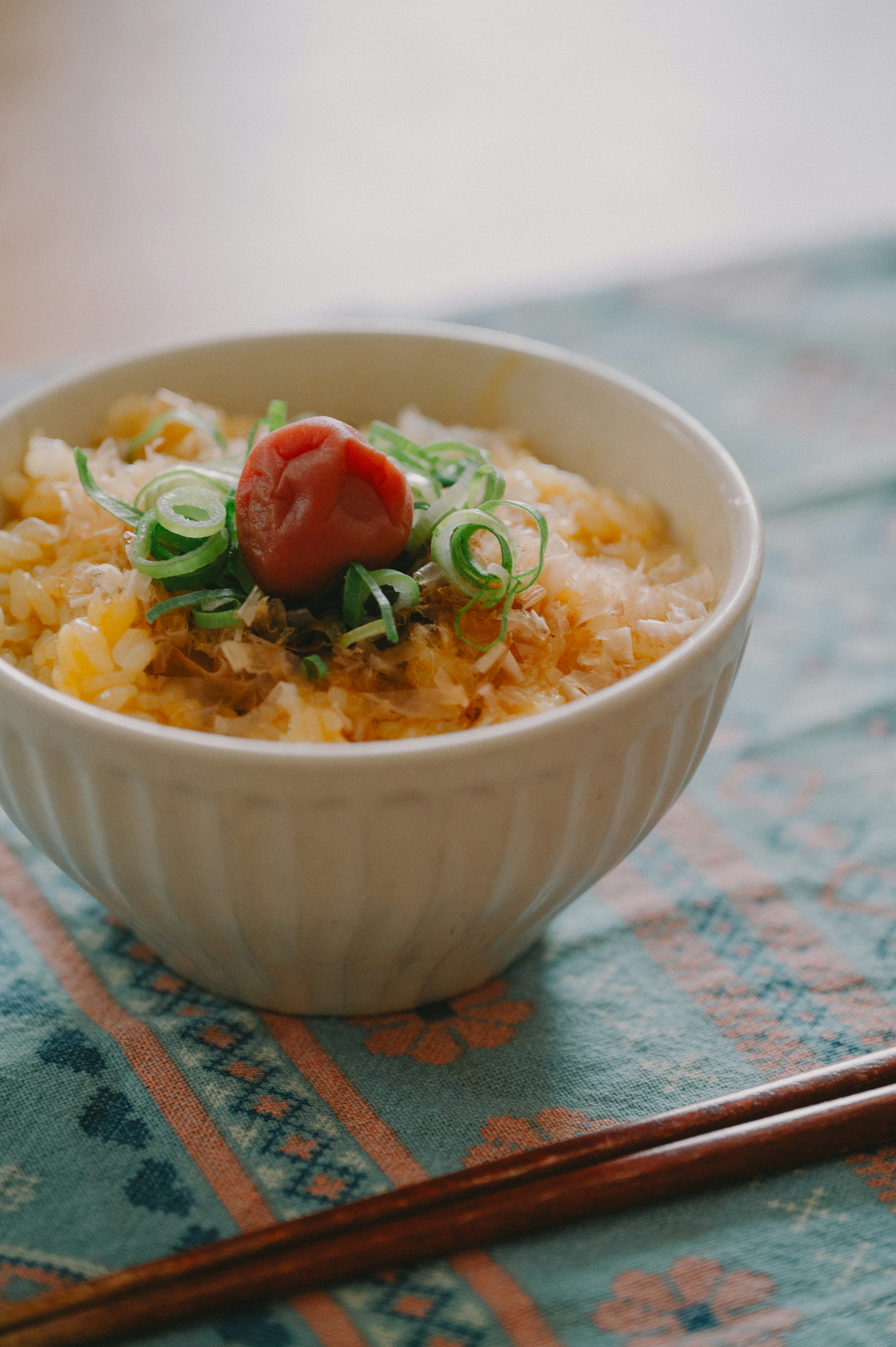 Rice dish in a white bowl topped with green onions and a pickled plum