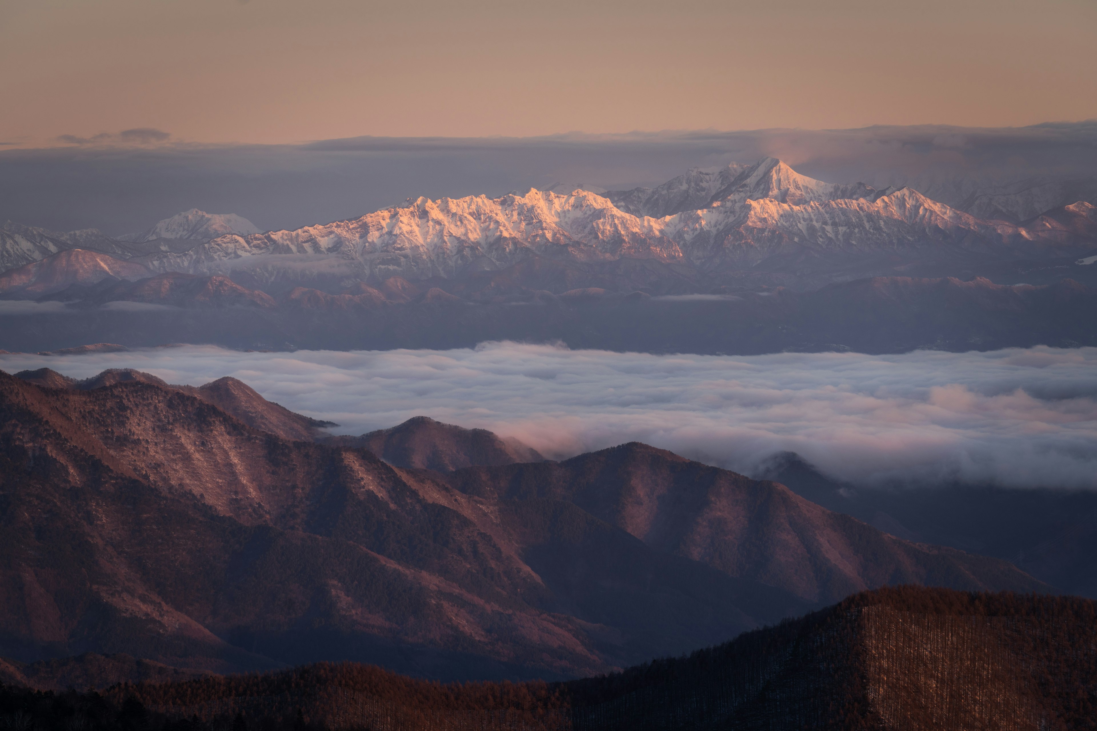 Catena montuosa panoramica con vette innevate sopra un mare di nuvole al tramonto