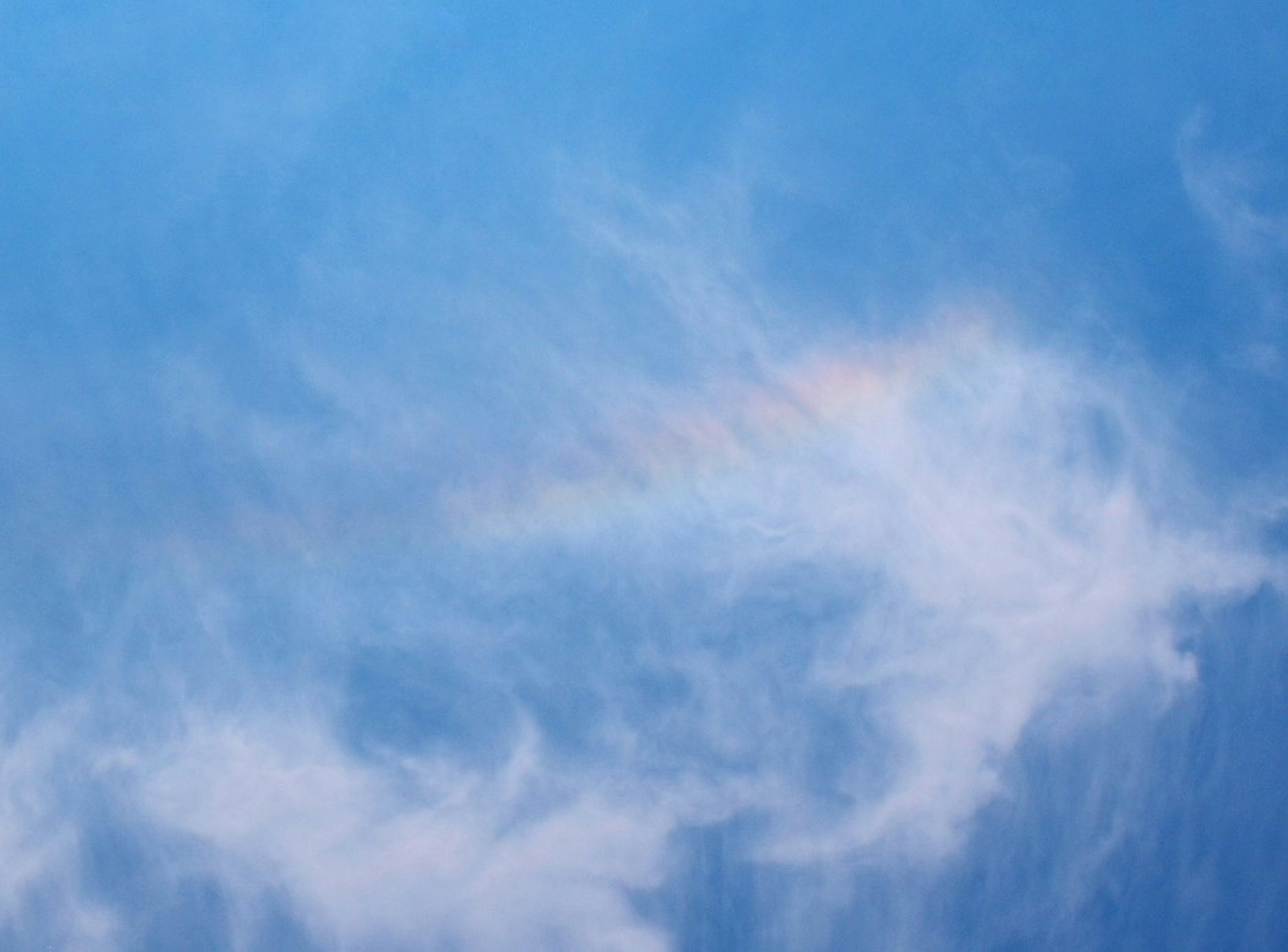 Nuvole sottili su uno sfondo blu con un accenno di arcobaleno