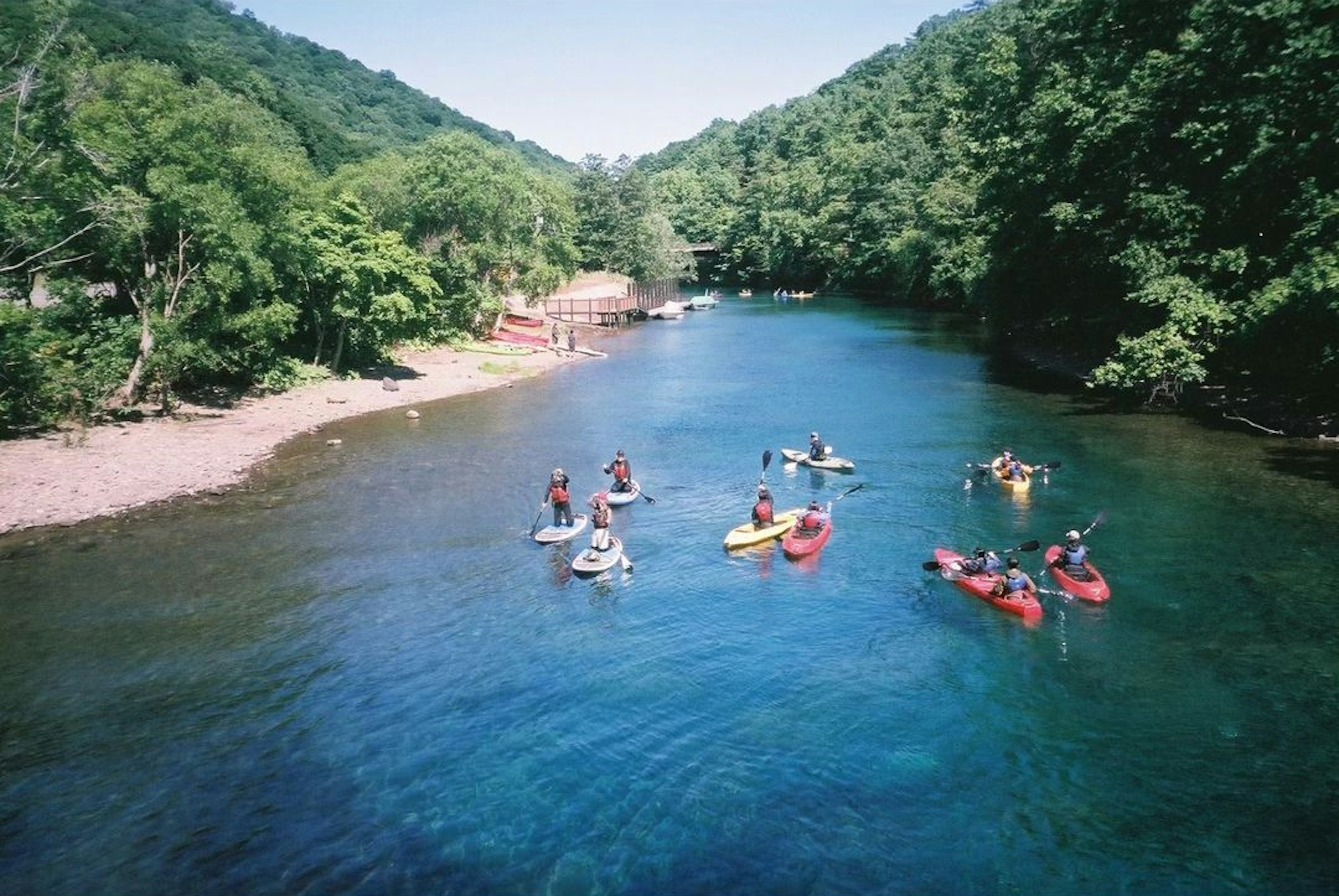 Menschen, die auf einem Fluss Kajak fahren, umgeben von Grün und klarem blauen Himmel