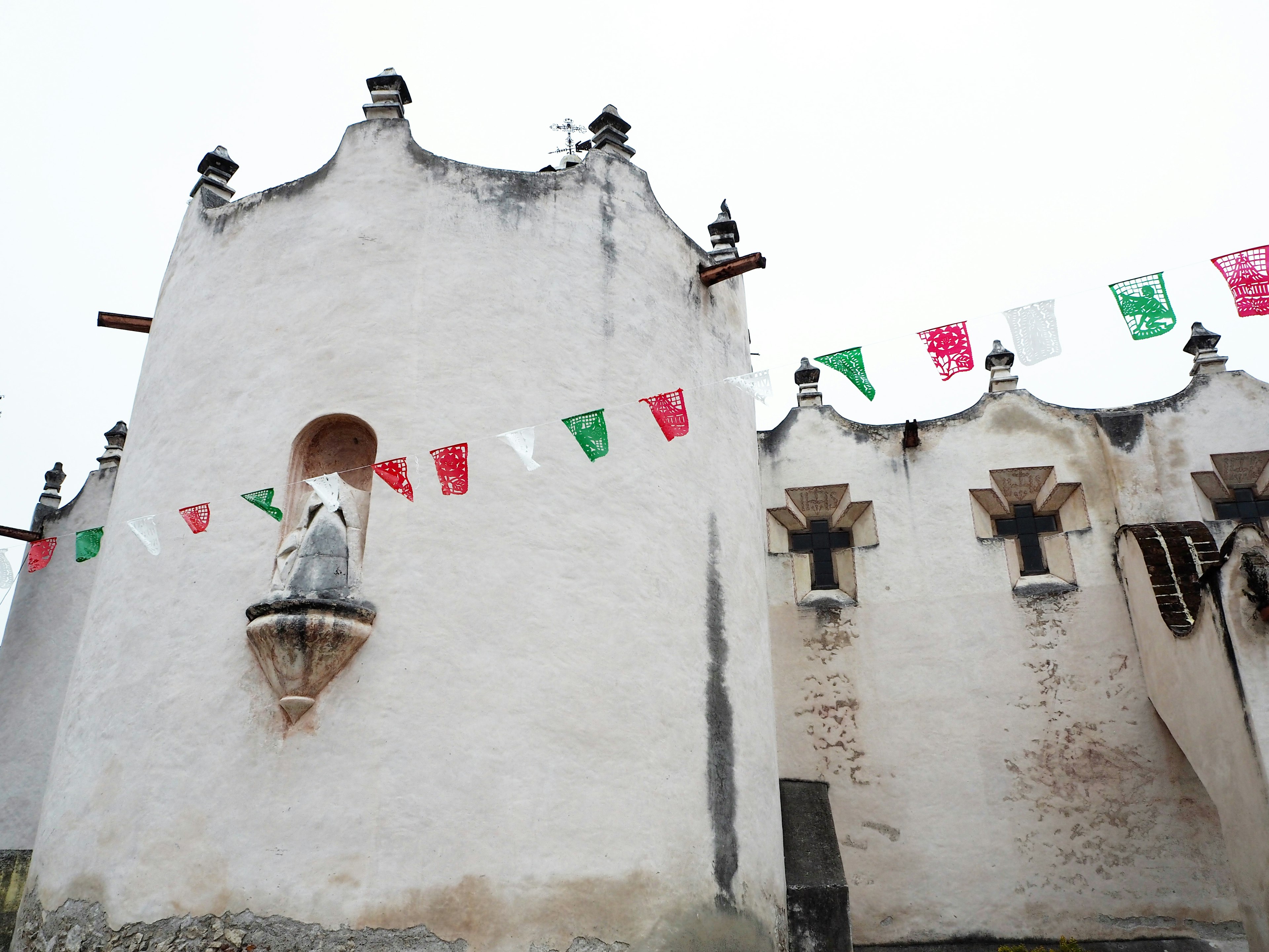 Exterior de una iglesia blanca con una estatua y banderas festivas