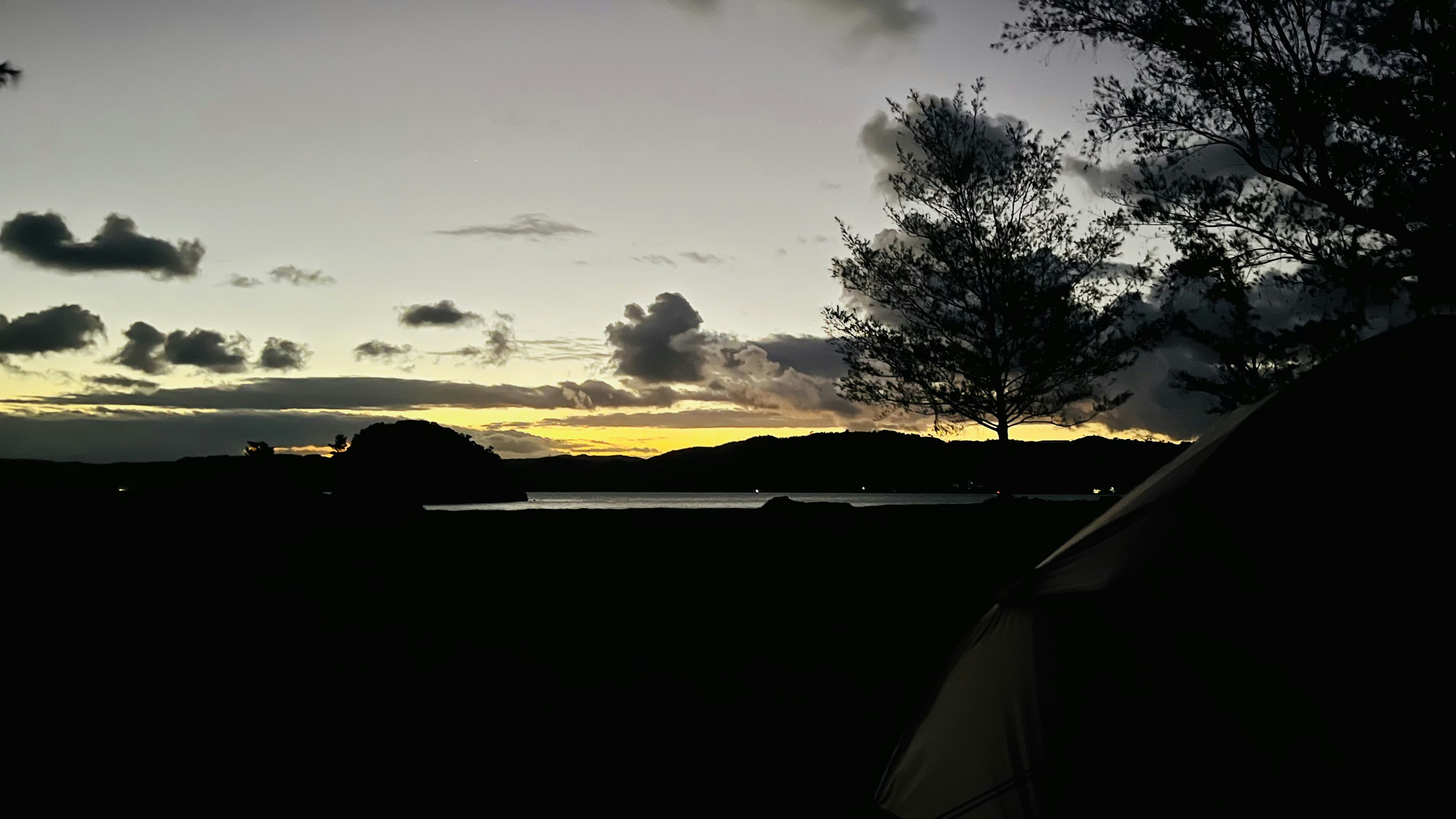 Beautiful landscape featuring silhouettes of trees and a tent along a sunset coastline