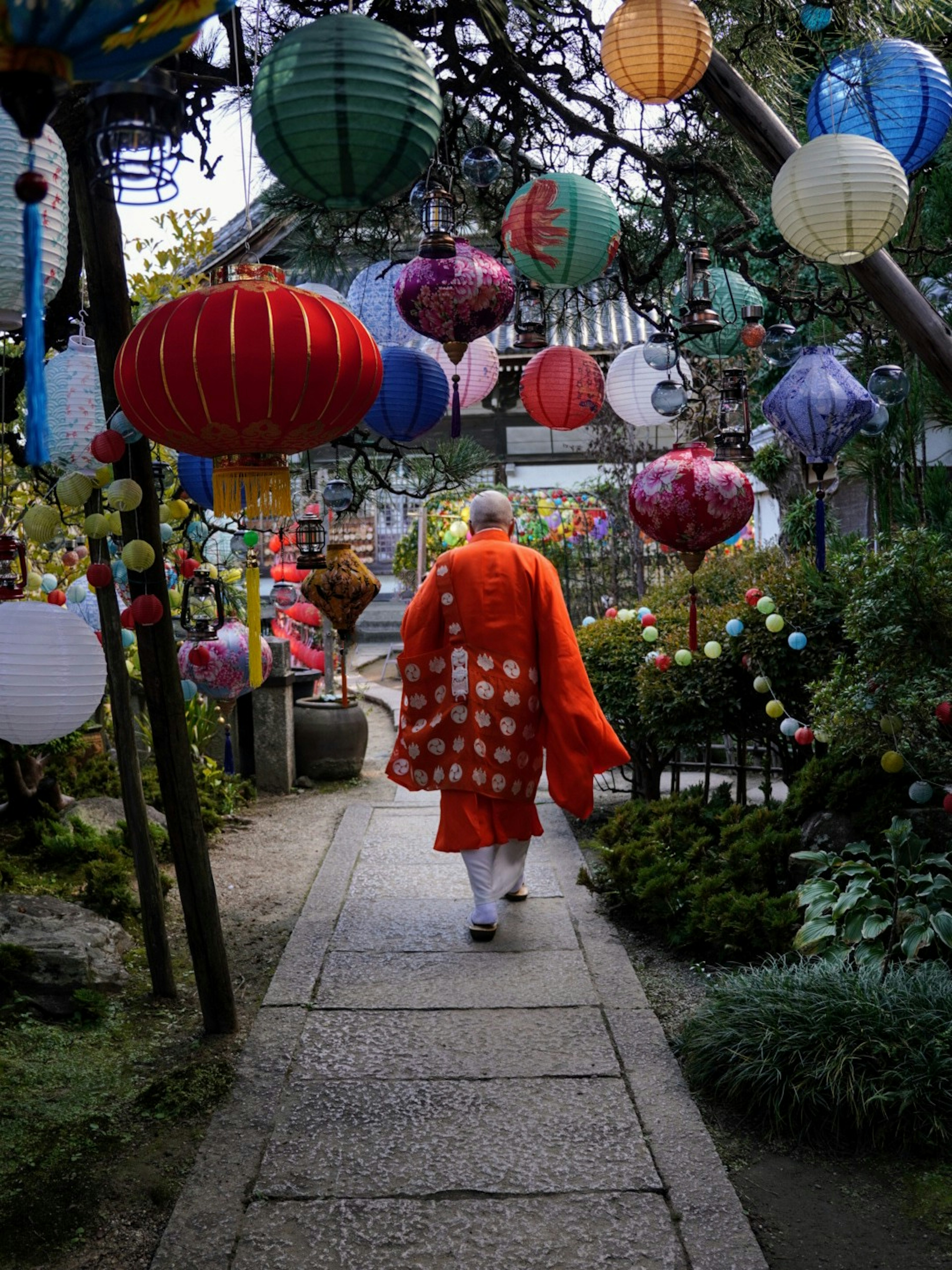 A monk in a red robe walking along a path surrounded by colorful lanterns