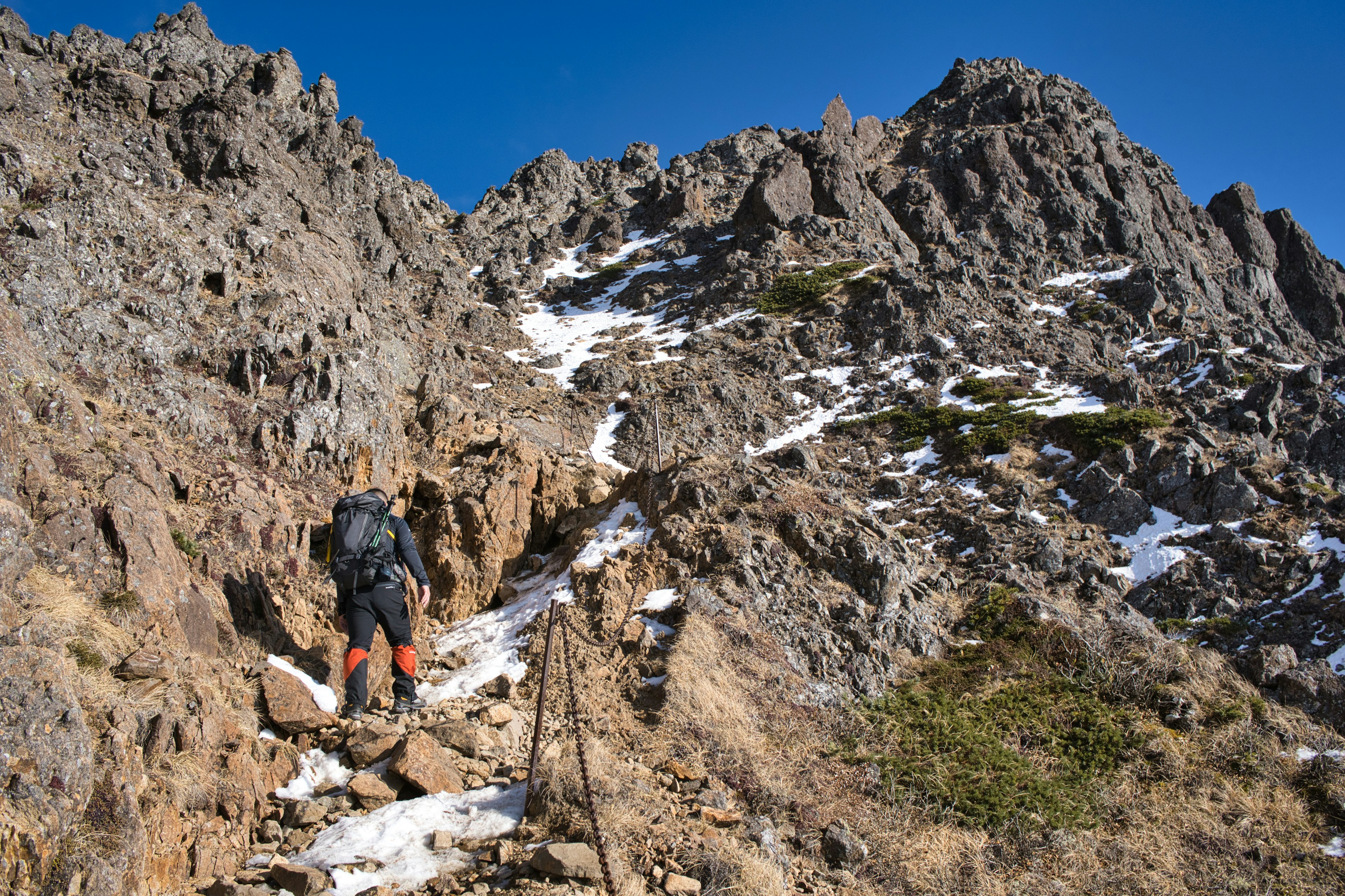 Wanderer, der felsiges Terrain mit Schneeresten erklimmt