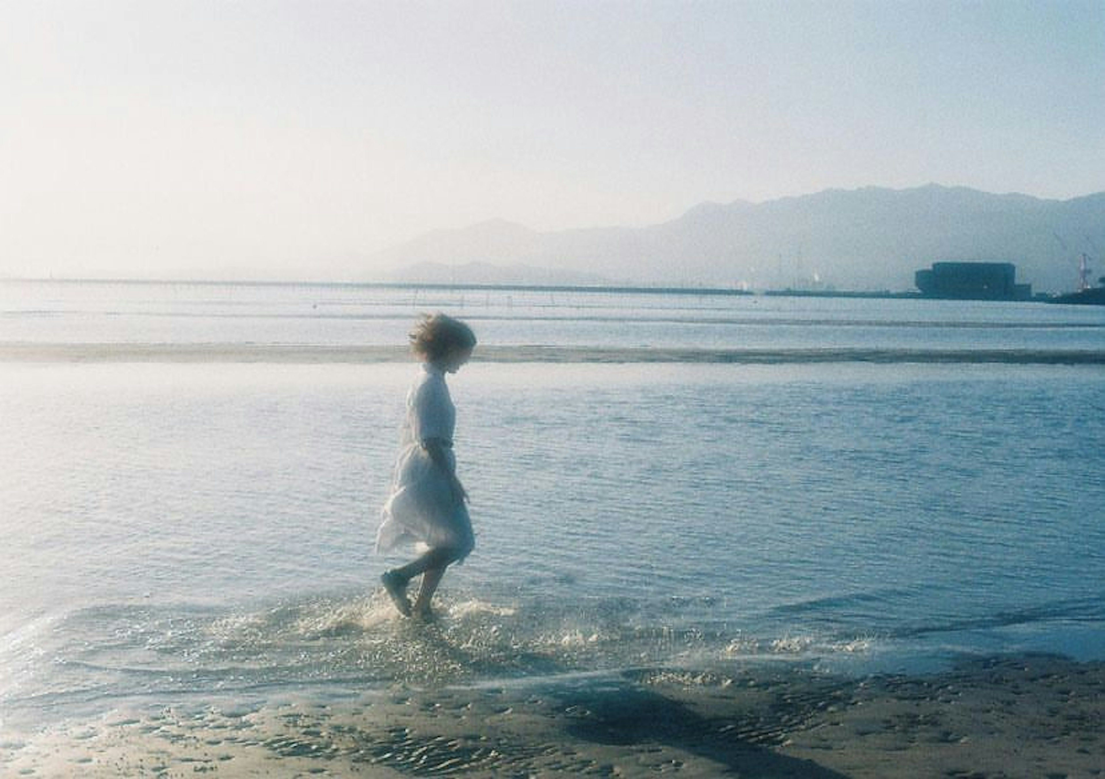 Una donna in abito bianco che cammina nell'acqua bassa sulla spiaggia