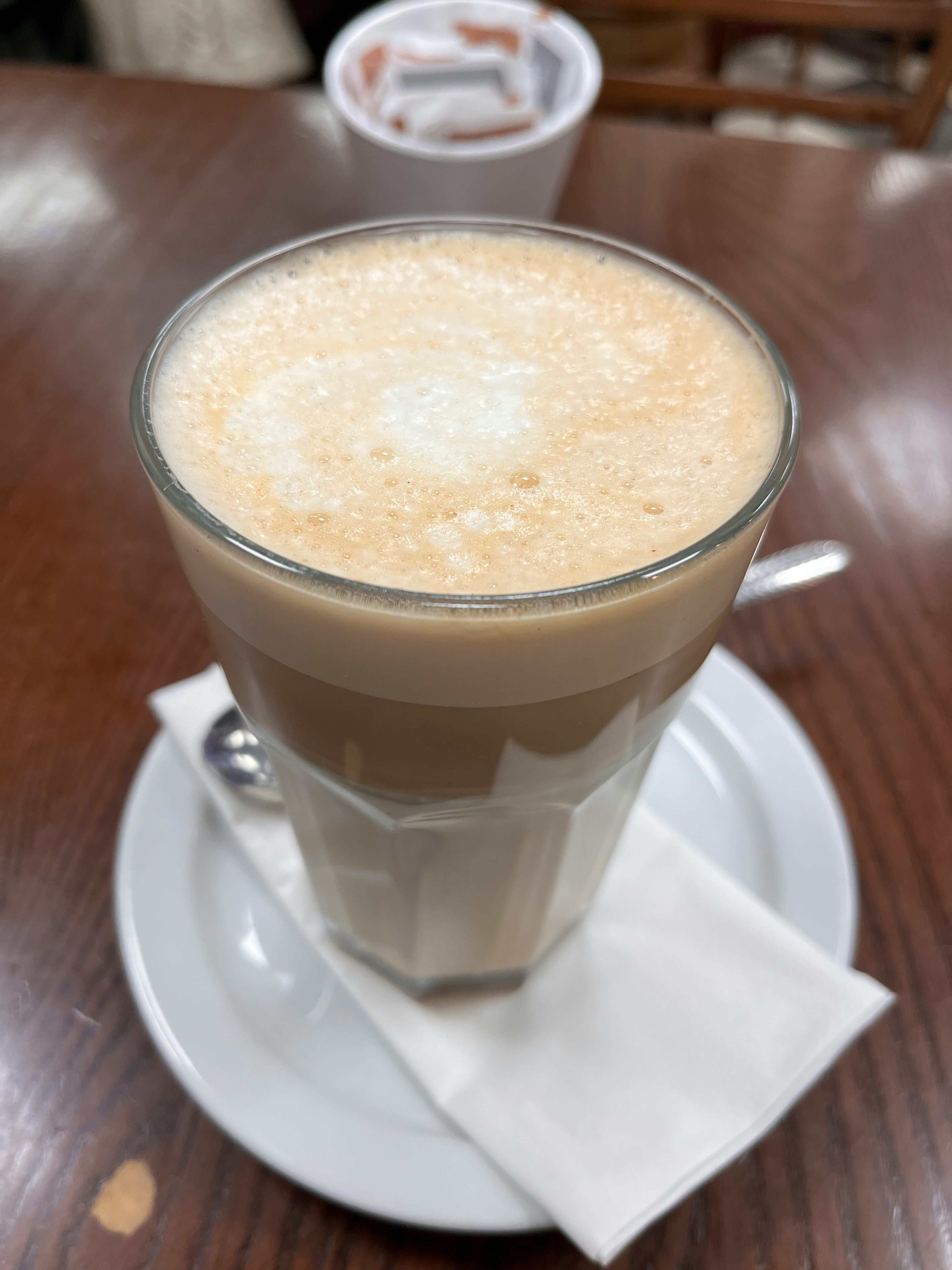 Glass of latte with creamy foam on top served on a white plate