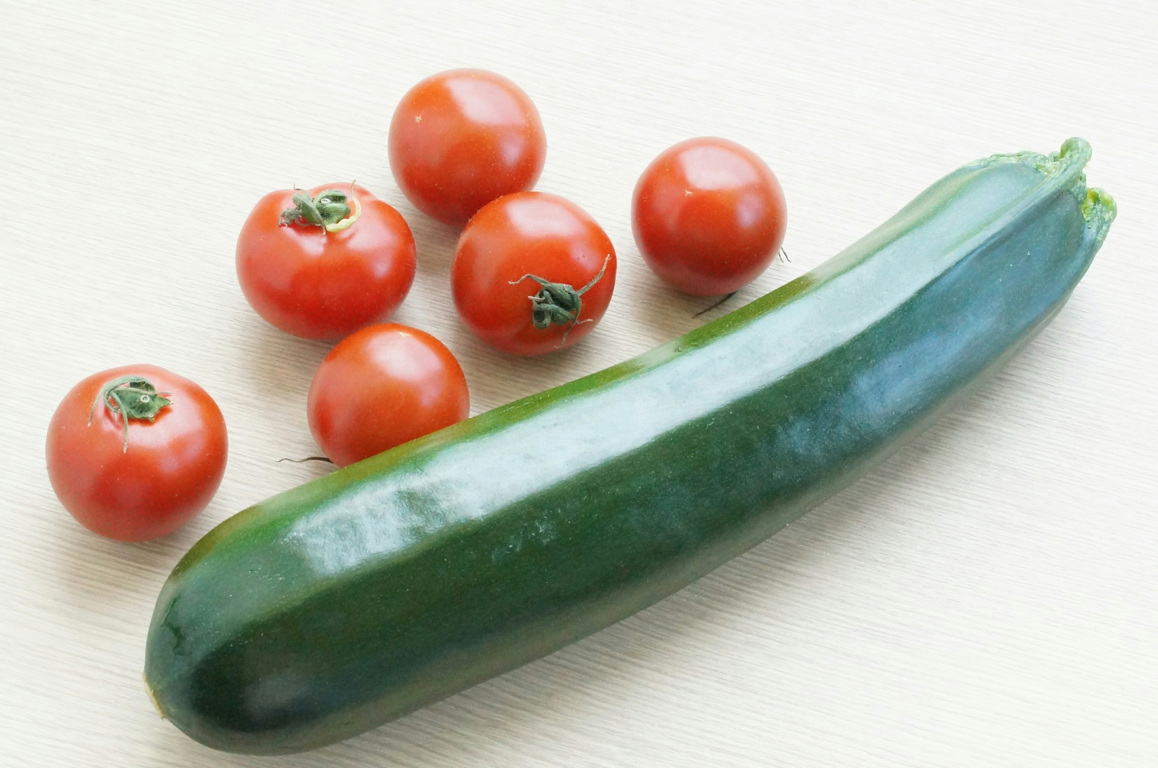 Una zucchina verde accanto a diversi pomodorini rossi