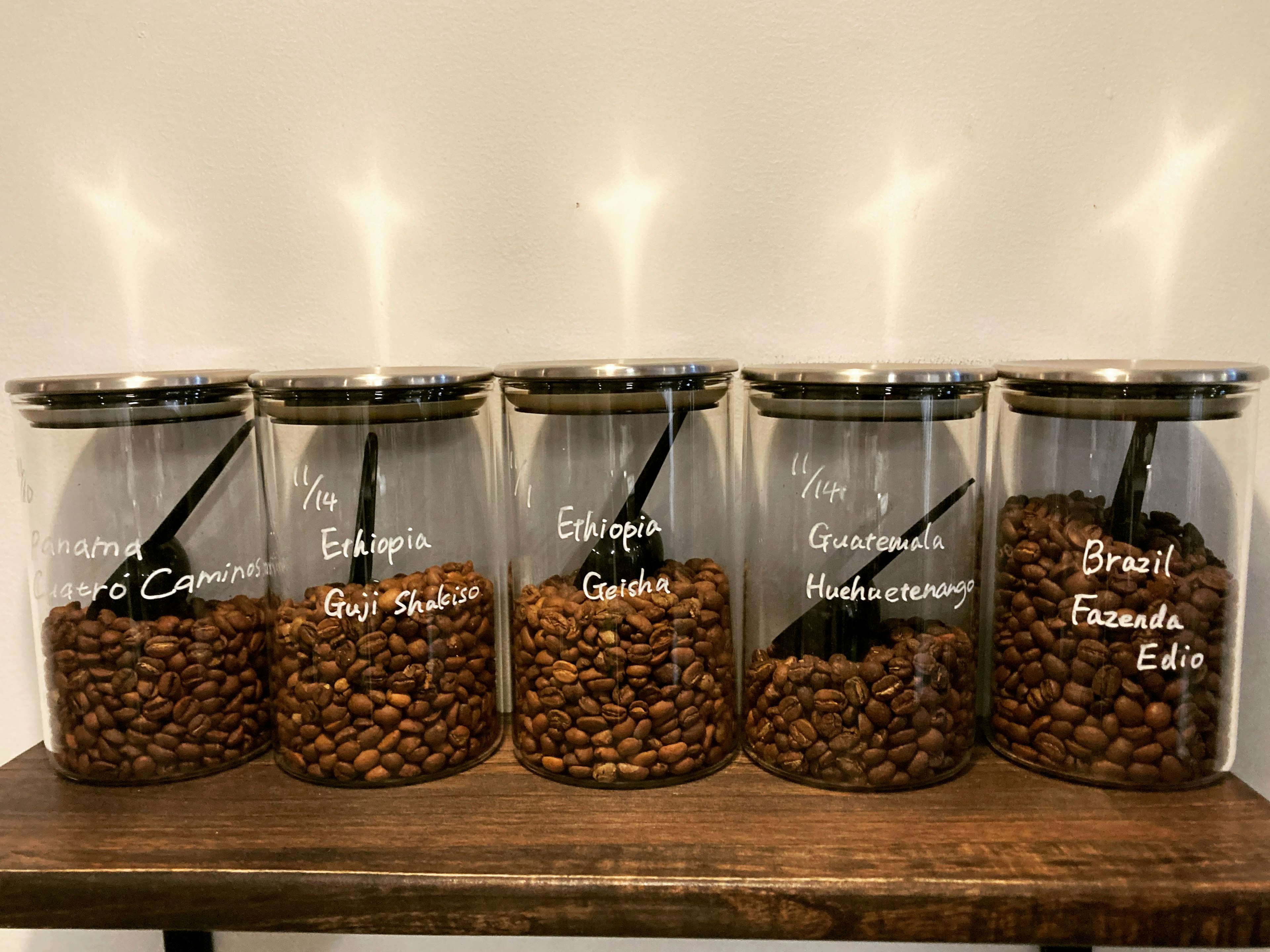 Bocaux en verre remplis de grains de café étiquetés par origine sur une étagère en bois