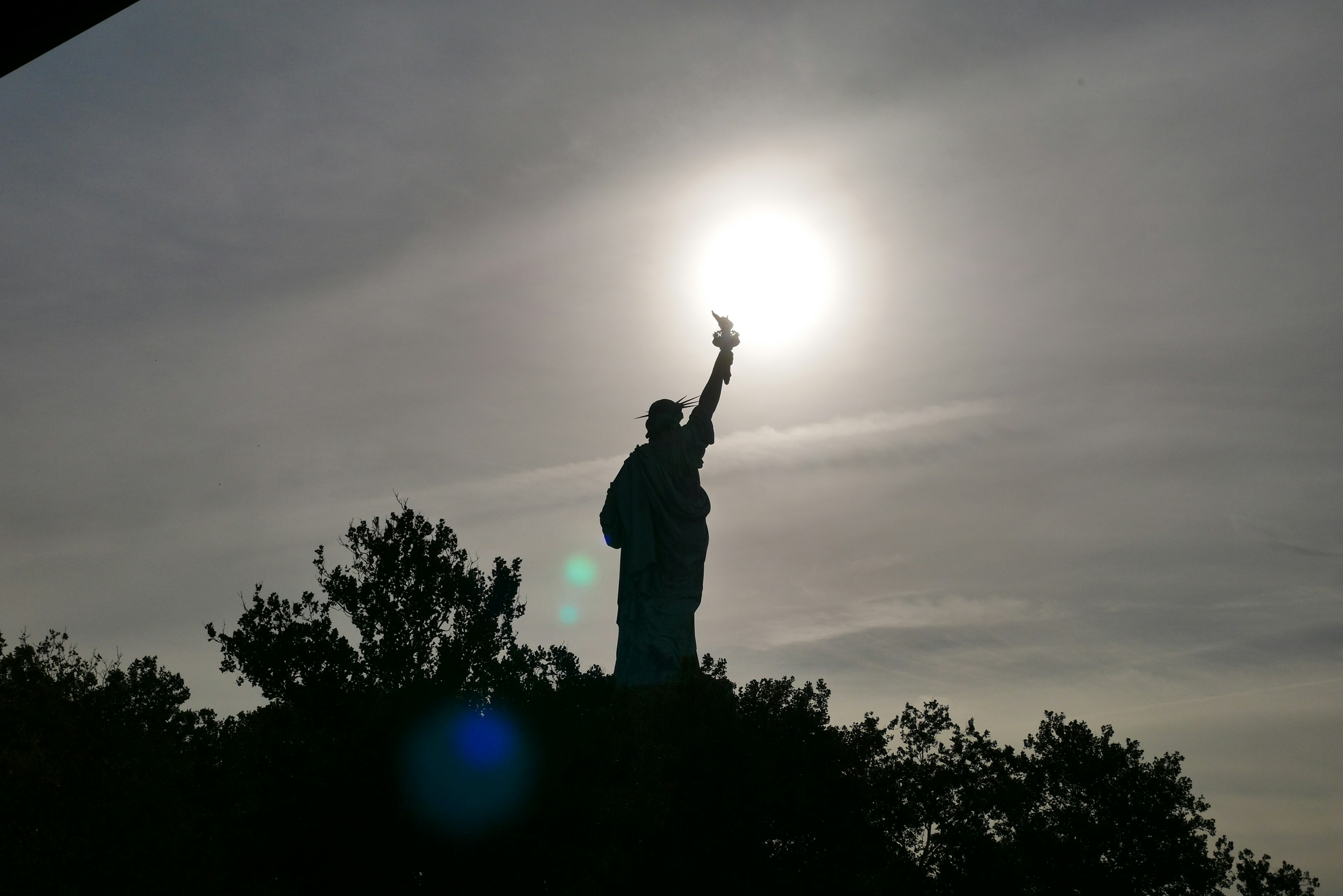 Silhouette of the Statue of Liberty against the sun