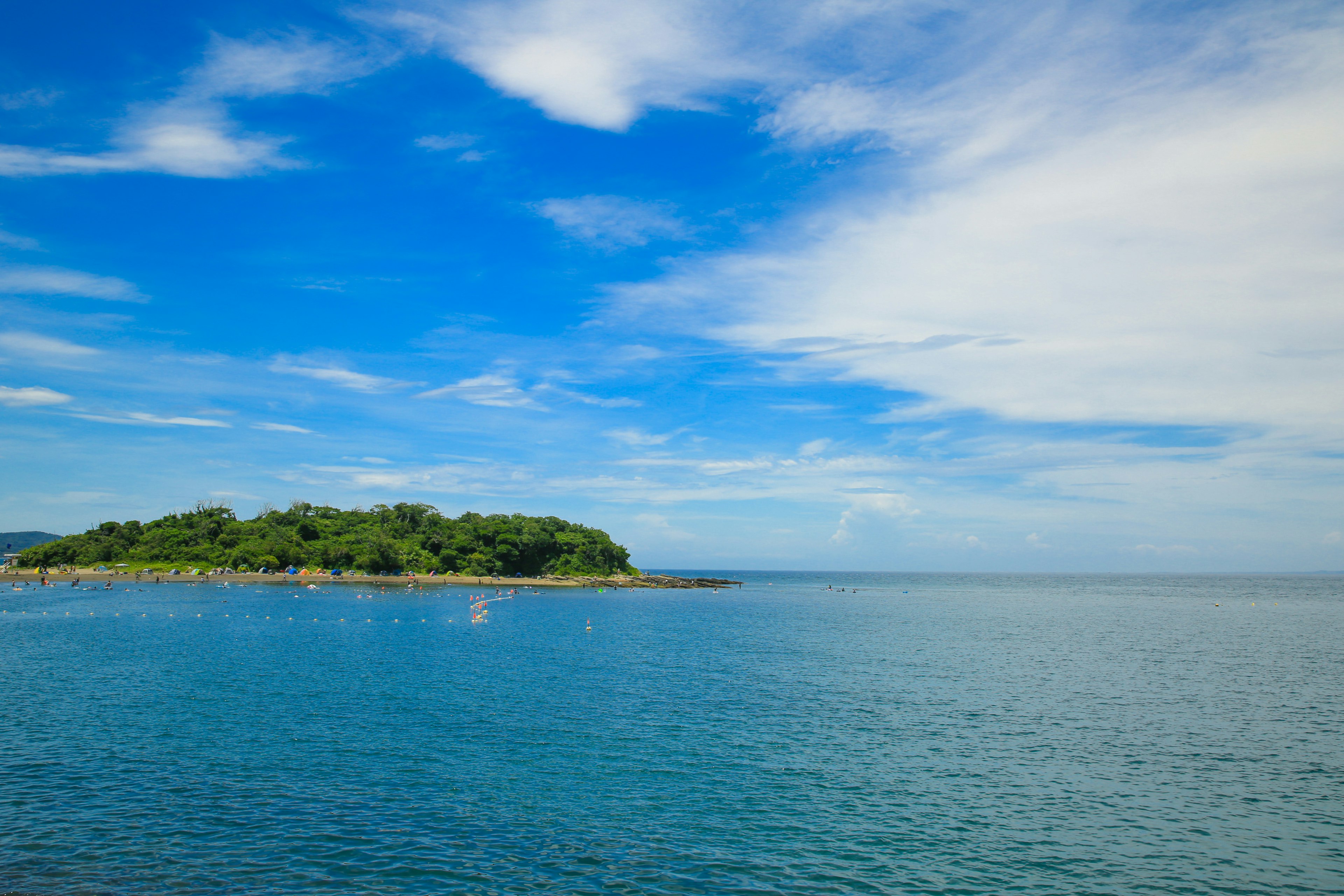 Eine grüne Insel umgeben von ruhigem blauen Wasser und klarem Himmel