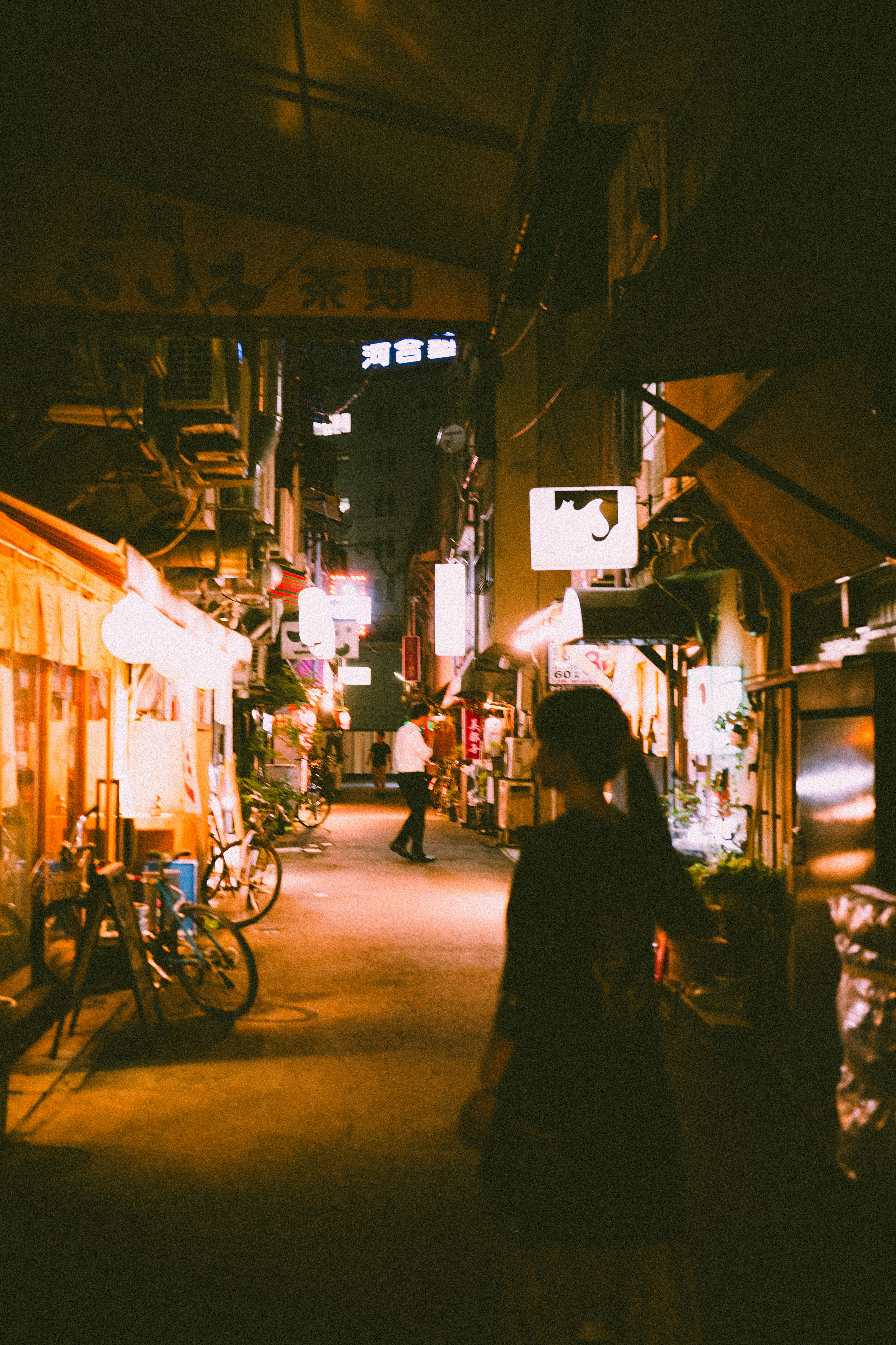 A woman standing in a street with warm lights and bicycles at night