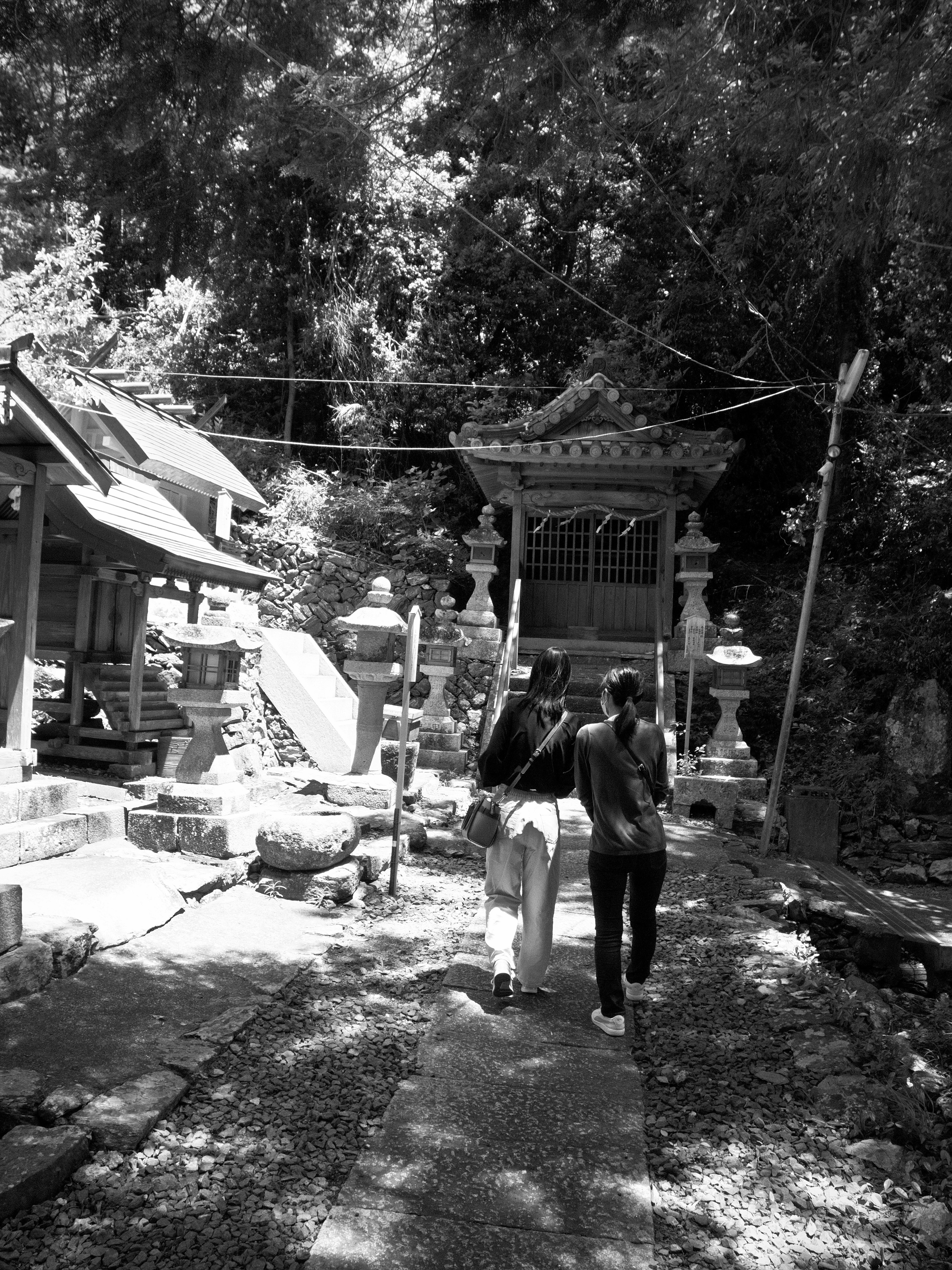 Two women walking down a path toward a shrine surrounded by lush greenery