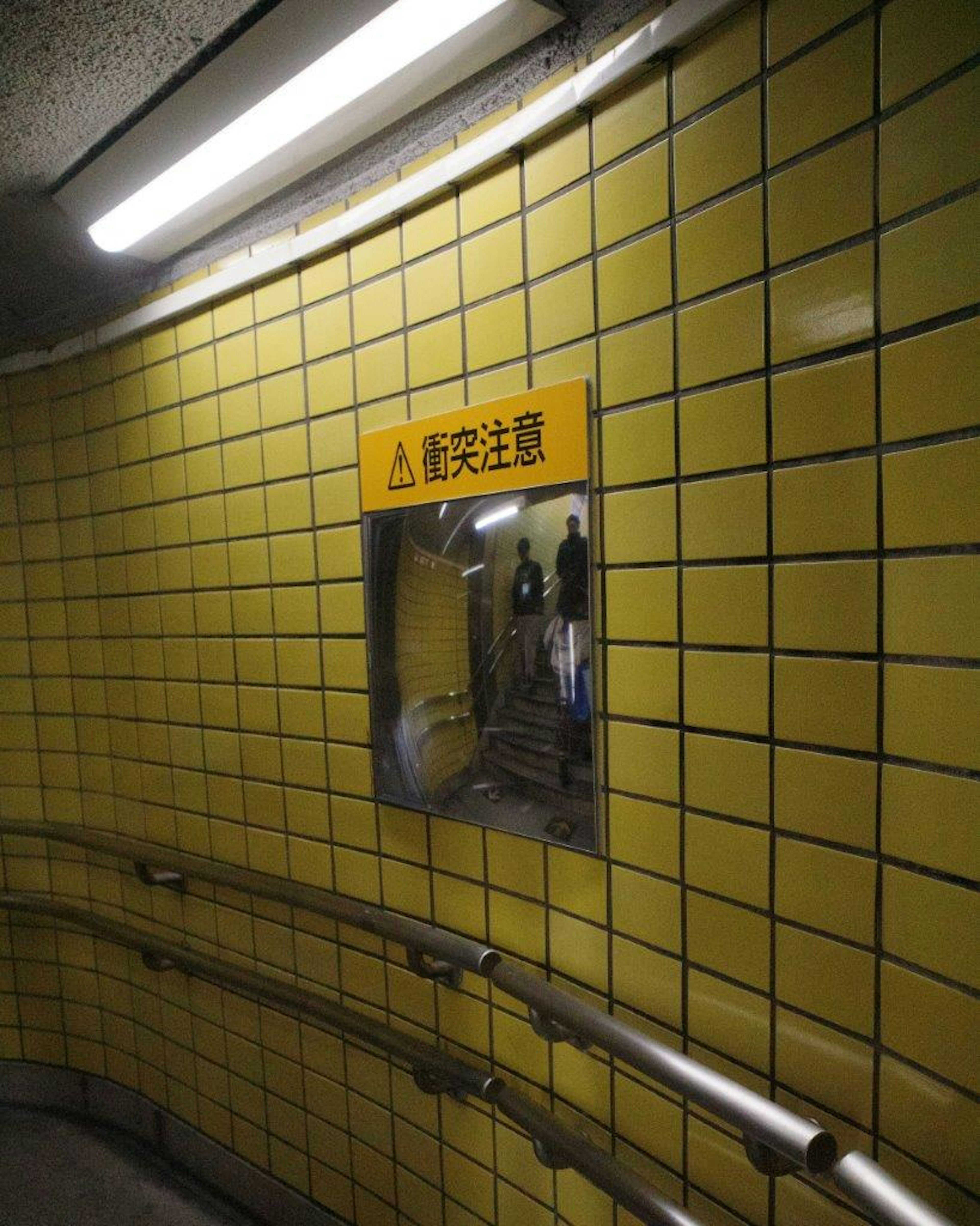 Yellow tiled wall in an underground passage featuring a warning sign