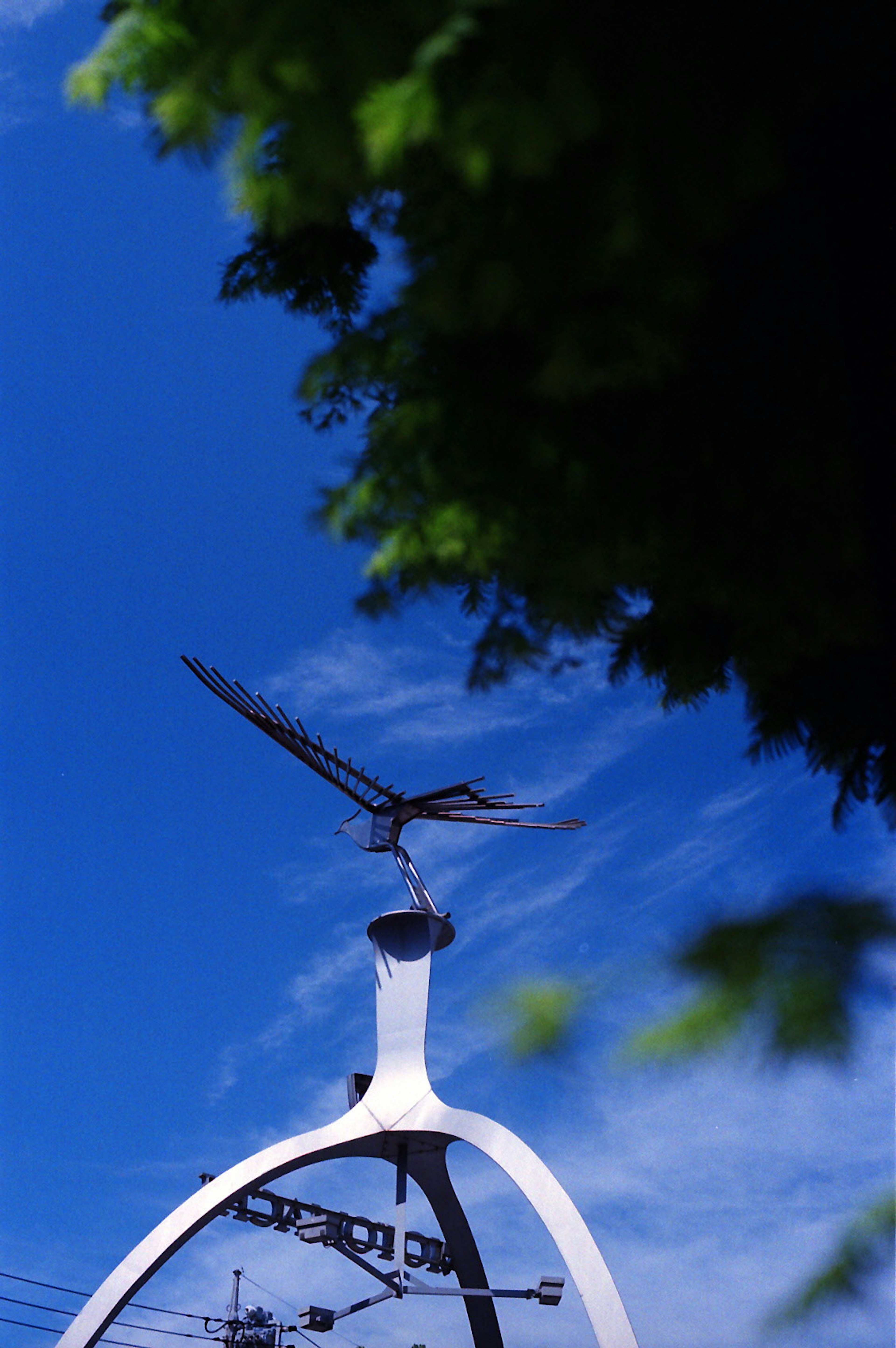 Sculpture of a clock with a bird design against a blue sky