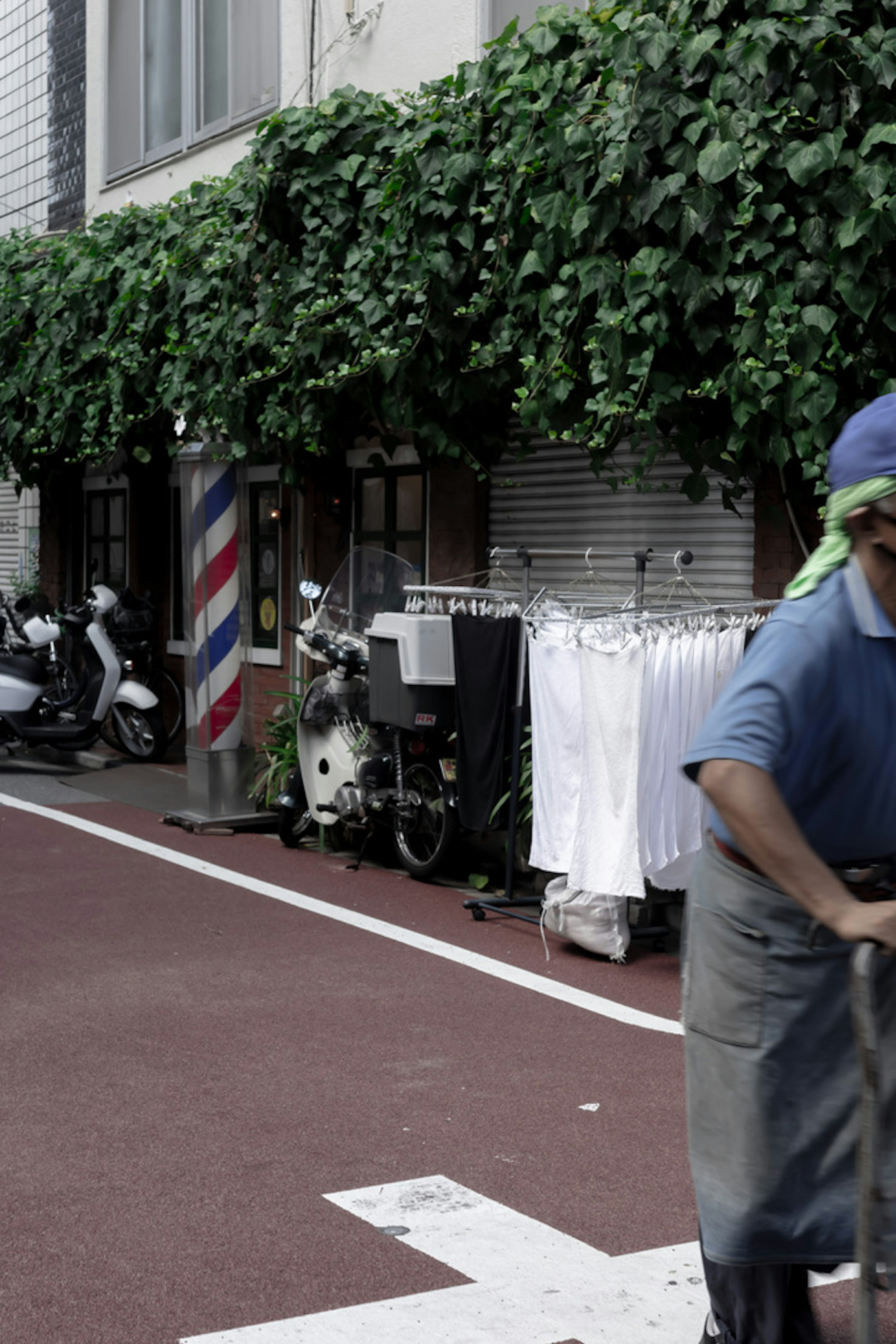 Un hombre trabajando frente a un edificio cubierto de hojas verdes y camisas blancas colgadas