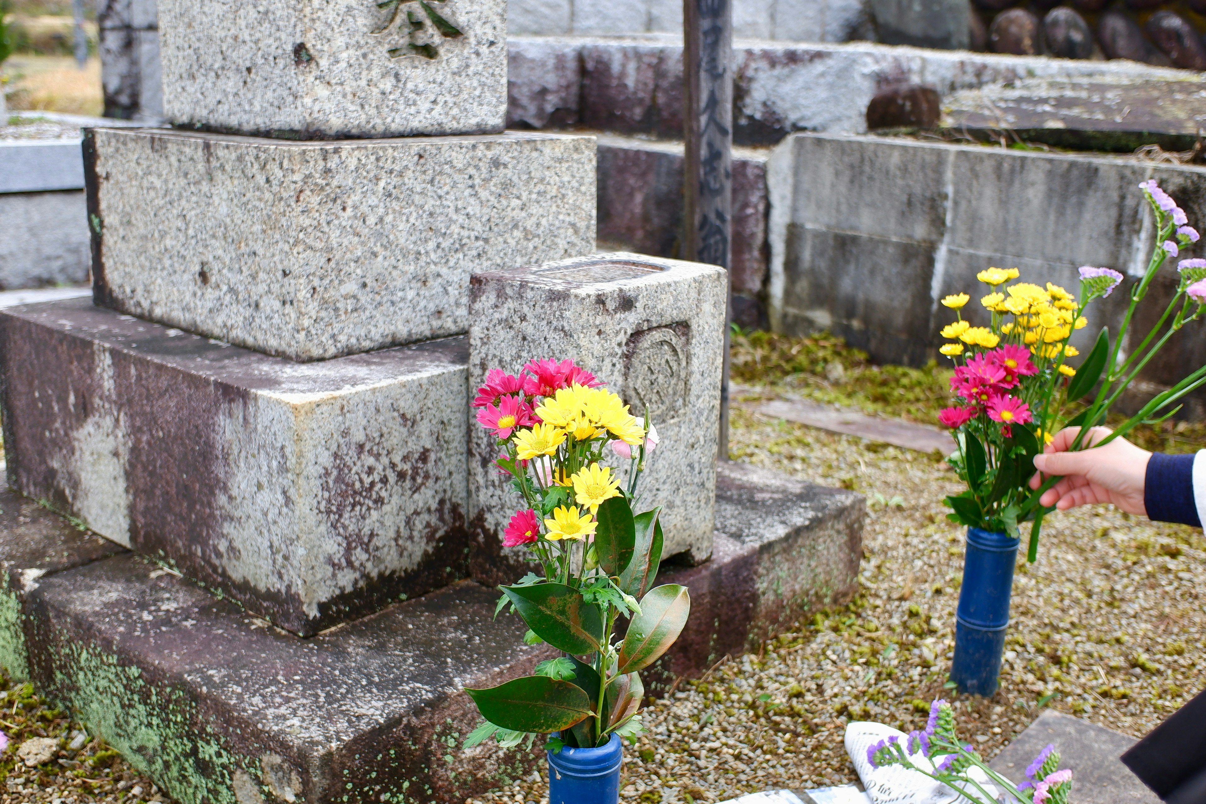 A person placing flowers at a stone grave in a cemetery