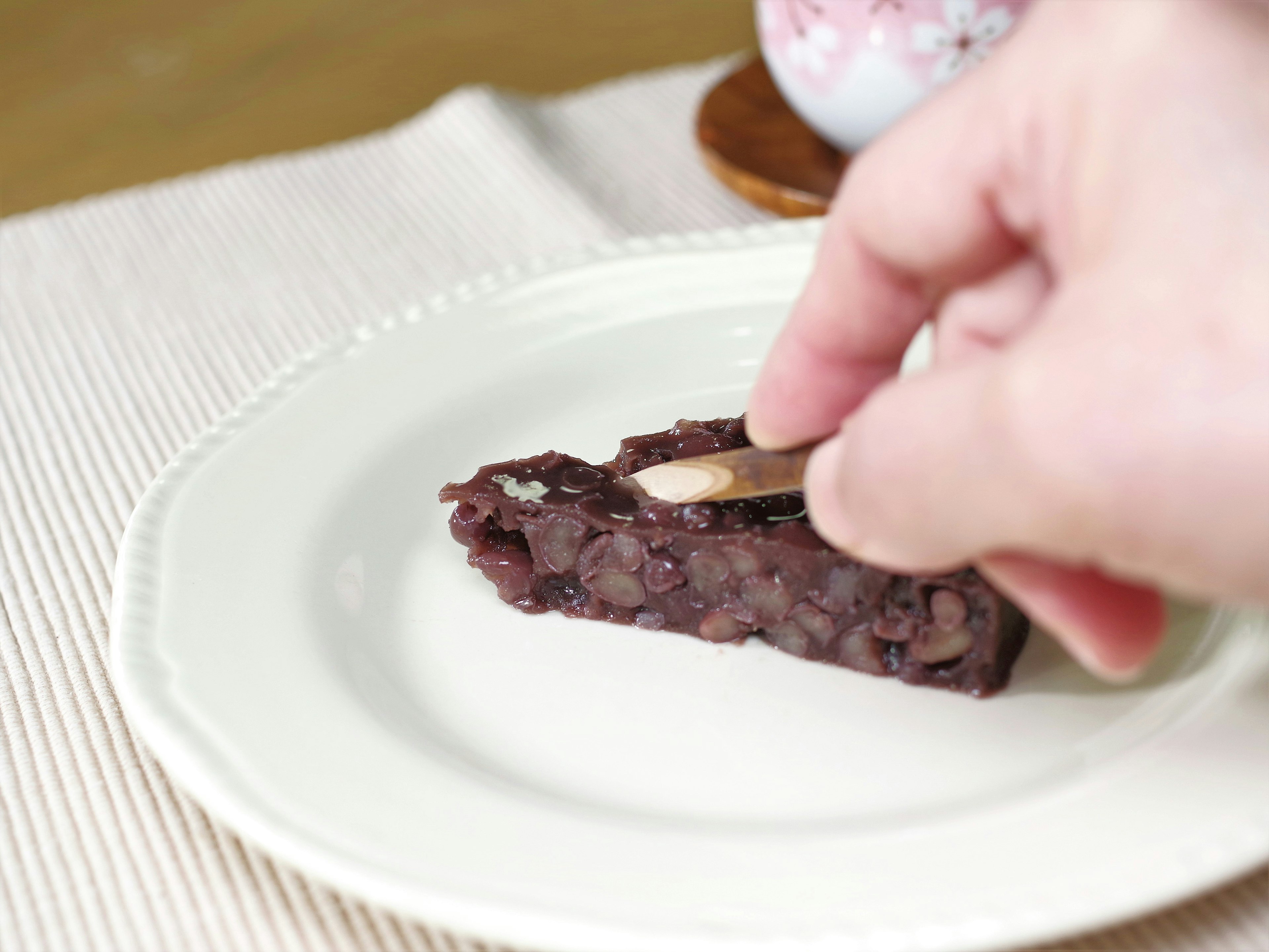 A hand picking up a slice of sweet red bean dessert on a plate