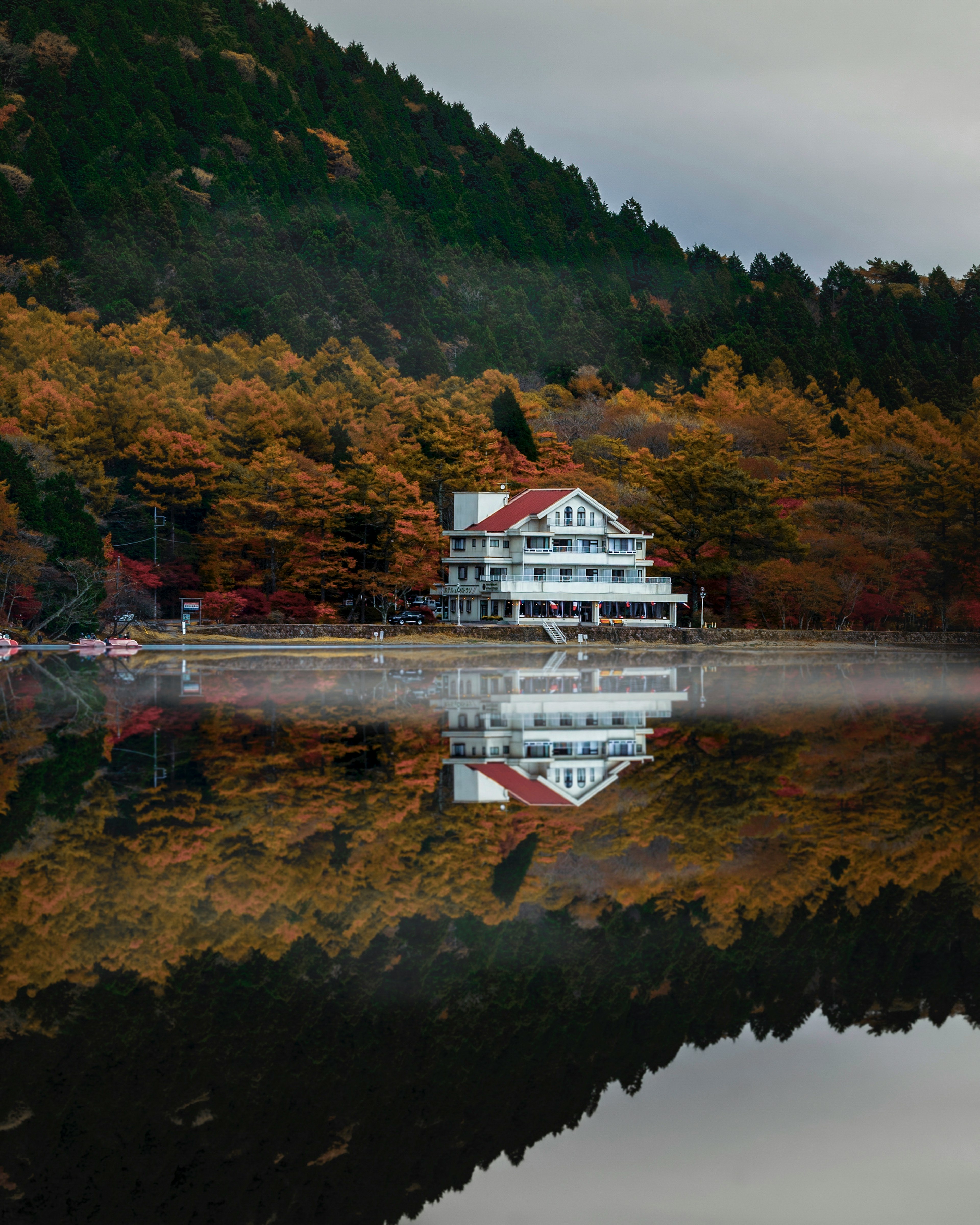 Weißes Haus spiegelt sich in einem ruhigen See, umgeben von Herbstbäumen