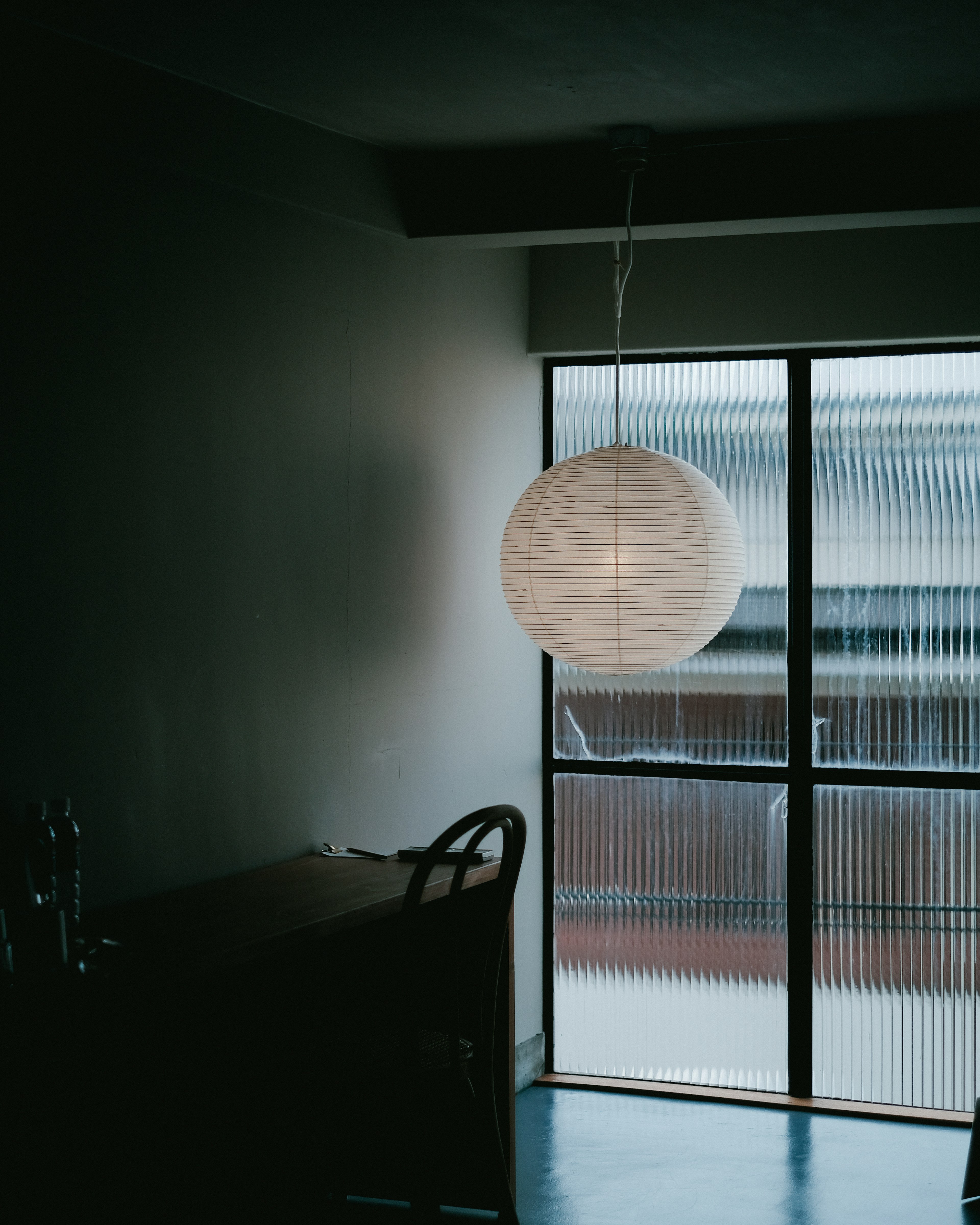 Corner of a room with a hanging white lamp and large window